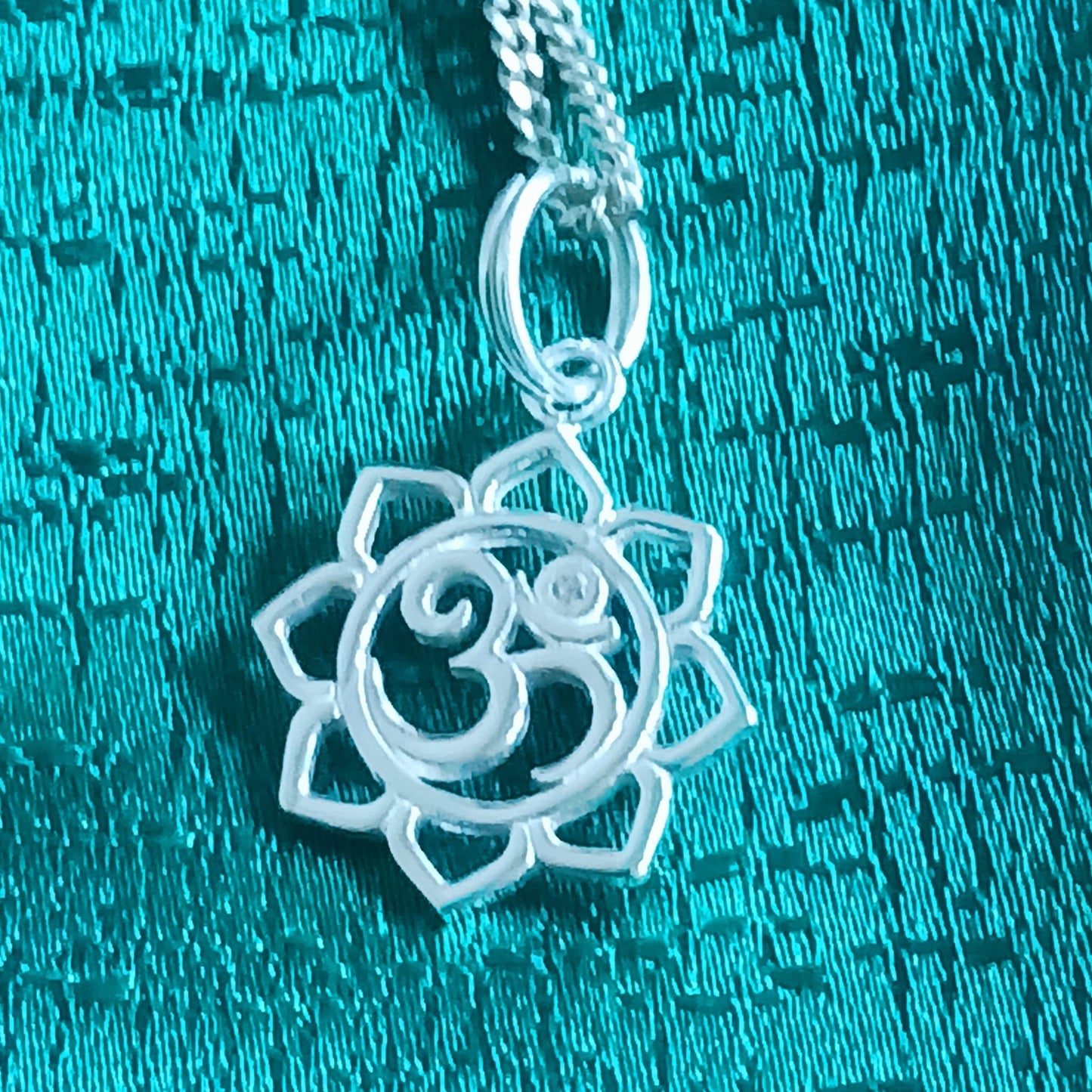 This lovely Om Symbol in Lotus silver pendant has a tiny embedded zirconia stone and comes with a fine solid 925 silver chain. Om or (Aum) is a sacred sound considered by many ancient philosophical texts to be the sound of the universe, encompassing all other sounds within it. In Sanskrit, om is called Pranava, which means to hum, and is considered an unlimited or eternal sound.
