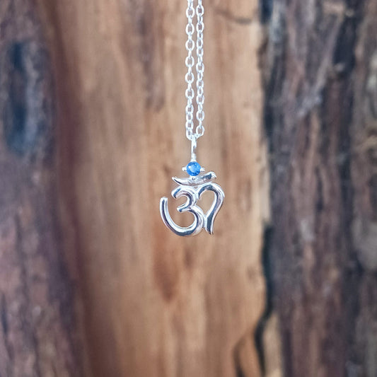 This lovely Om Symbol silver pendant is very dainty and comes with an inlaid Corundum blue stone, on a fine solid 925 silver chain. Om or (Aum) is a sacred sound considered by many ancient philosophical texts to be the sound of the universe, encompassing all other sounds within it. In Sanskrit, om is called Pranava, which means to hum, and is considered an unlimited or eternal sound.