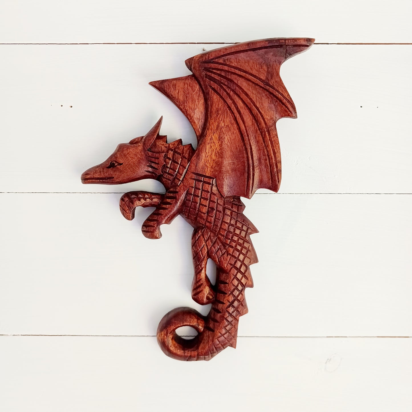 This intricately carved Dragon plaque sit flush against the wall or can be hooked onto pots or some other items in the home. These Dragons are hand carved with metal hook for hanging if you choose. In early cultures, the dragons were often seen as mighty serpents and beasts that were either extremely benevolent or fearsome and difficult to kill. The beliefs of a region are often influenced by geographical location. Eastern cultures often saw dragons as a knowledgeable deity that had power over storms