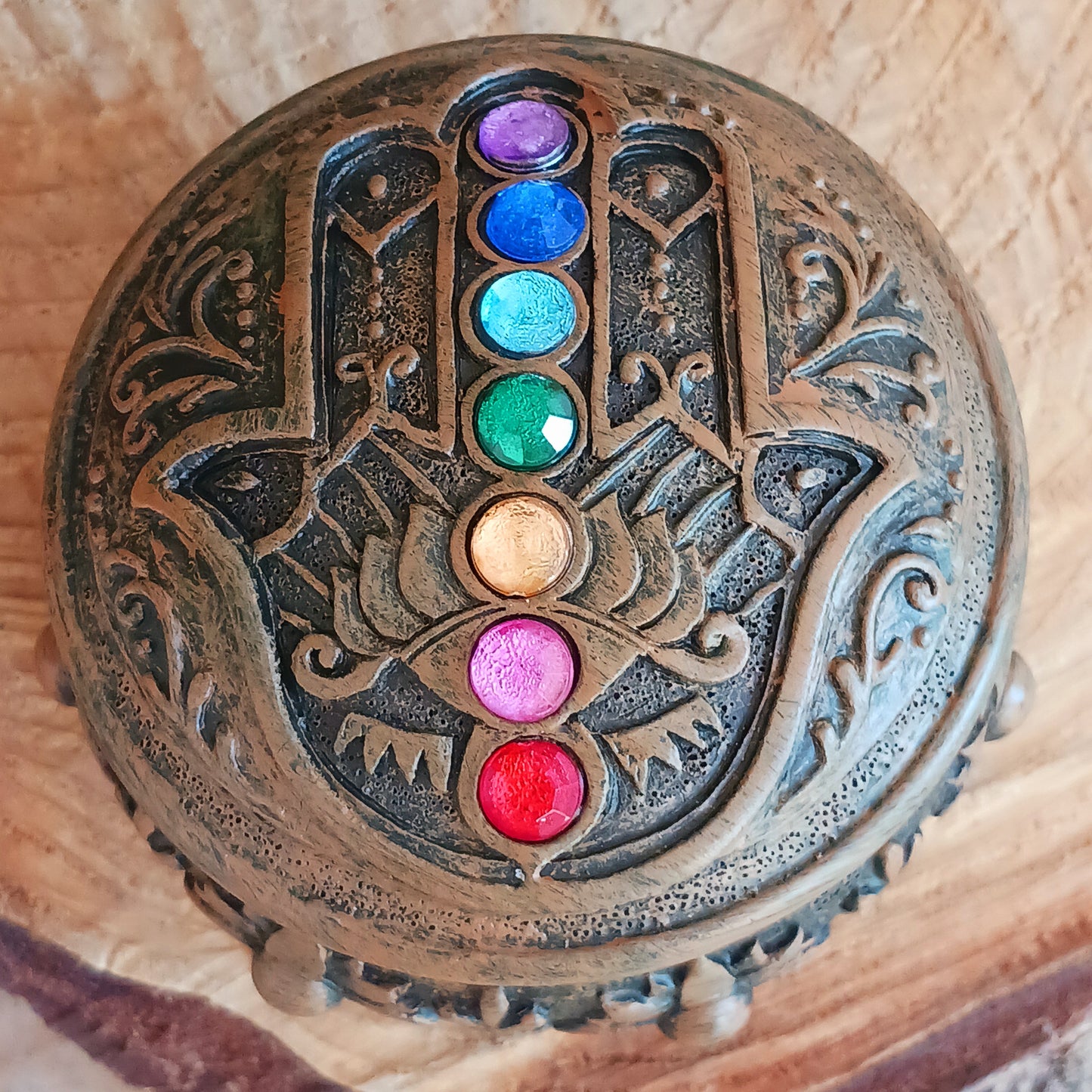 This beautiful Charka Box features Hamsa's Hand which is known for offering protection and happiness to its owners, you can rest assured that your most prized possessions are safe from prying eyes. With engraved flowers and patterns around the side of the box, and finished with coloured gemstones on the top of the lid. This piece is perfect for anyone who needs a little protection in their life.