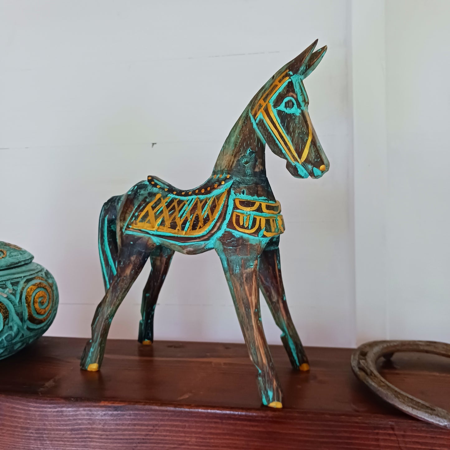 Add a touch of exotic equine elegance to your home with this beautiful hand carved decorative horse figure. Handcrafted from high-quality albasia wood in Indonesia, this striking piece features intricate carvings highlighted in gold and turquoise accents, creating a stunning contrast.