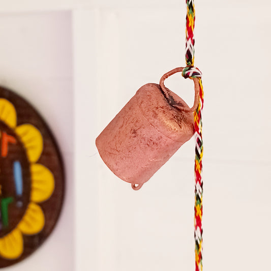 String of small rustic handmade ironwork bells with copper coloured paintwork, hung on a length of colourful string. Each bell has a small metal clapper which produces a gentle tinkling sound.