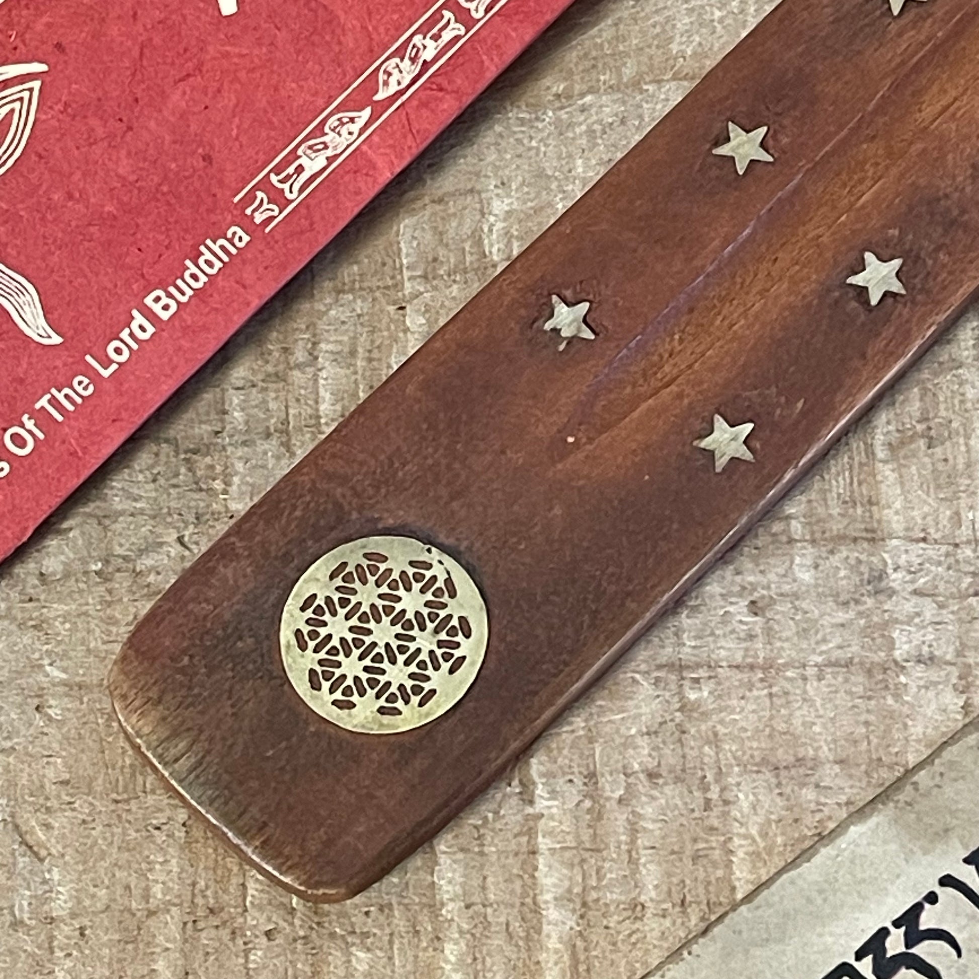 This popular shoehorn-style incense holder, crafted from mango wood, serves as both a beautiful and functional ash catcher. The design is adorned with brass inlays featuring stars and the Flower of Life, a symbol representing the interconnectedness of life. Its long, slightly curved shape securely holds stick incense, with the wooden base effectively catching falling ash to keep surfaces clean.