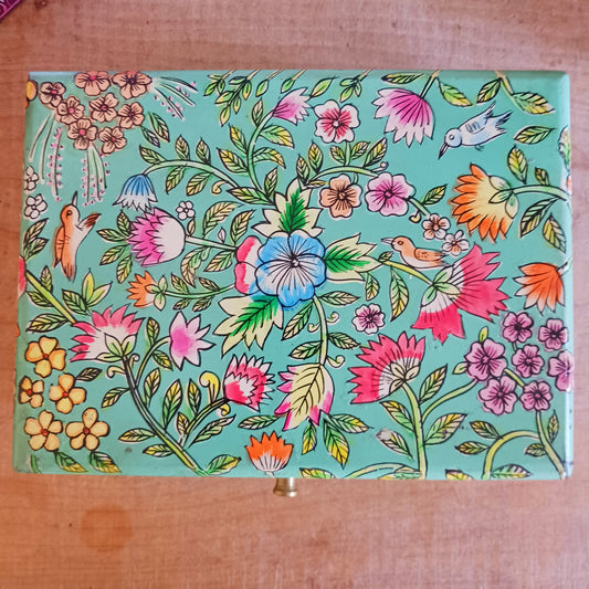 The Saanvi Handcrafted Large Wooden Box is a sustainable gift of beauty, designed to bring charm and practicality to any space. Expertly hand-painted in a bright mixed floral pattern on a pale blue background, this decorative box exudes artisanal elegance. The hinged lid is accented with a small gold-colored knob for a refined touch, while the deep midnight interior offers ample storage for trinkets, jewellery, and cherished keepsakes.