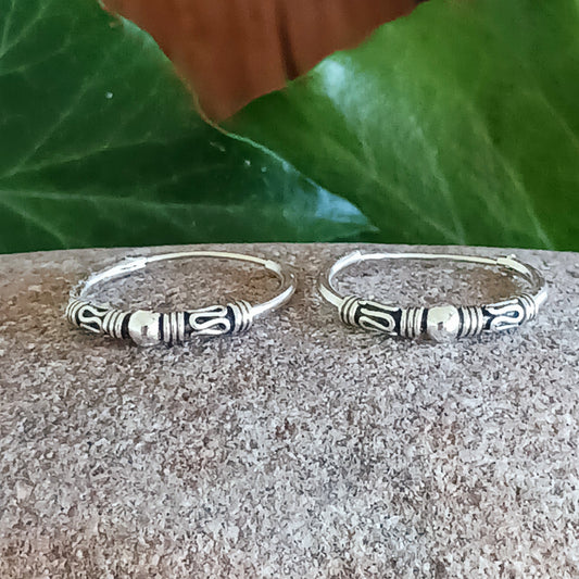 These sterling silver hoop earrings showcase a stunning Bali-inspired design, perfect for adding a touch of elegance to your boho-chic style. The intricate craftsmanship features a delicate silver ball accent at the center of each hoop, embodying a timeless and versatile aesthetic.