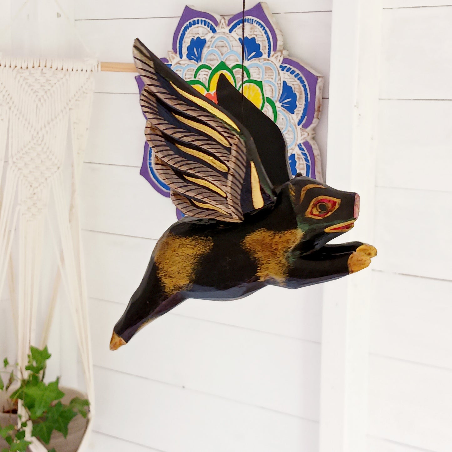 Invite protective energy and traditional charm into your home with this handcrafted Flying Pig Spirit Guardian from Bali. Known locally as a "Cradle Guardian," this winged figure is believed to ward off negative entities and is often placed in temples or homes, suspended from elevated areas like doorways or windows. Its downward-facing posture channels protection, while the strong twine loop allows for easy hanging.