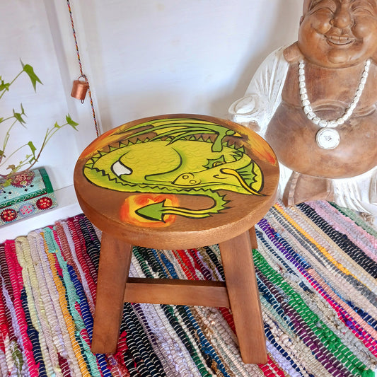 This lovely little handmade, carved and painted stool is Fairtrade from Thailand. The top of this stool has been carefully hand carved and then painted to show a peacefully curled, sleeping dragon surrounded by flames. These cheeky little items are very versatile making great stools for little bums or as tiny tables to add accent to your home. They can also be very useful as a step for those hard to reach high up shelves or even just to put your feet up on, and due to their small form are easy to store.