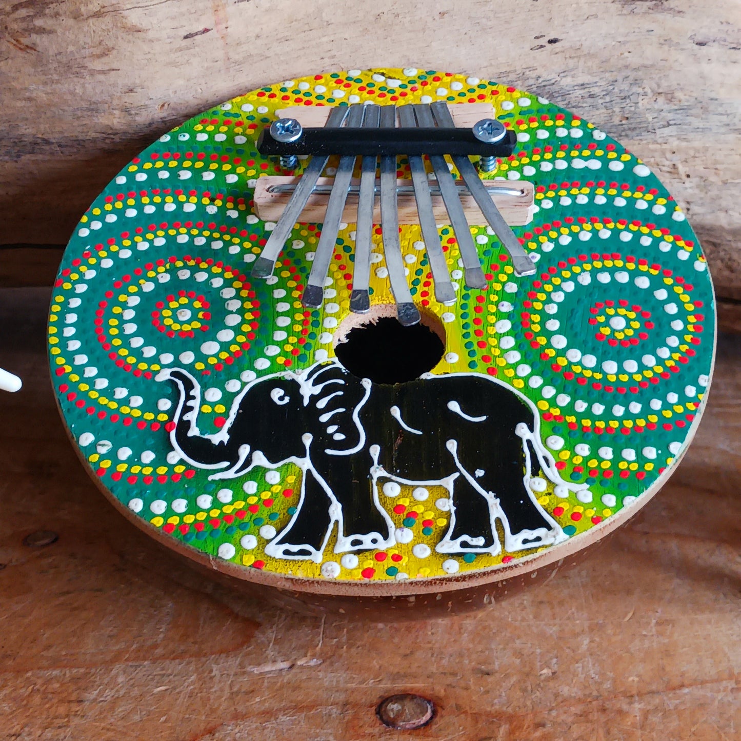 This thumb piano has been hand carved out of coconut shell and decorated with vibrant colour dot painting of an elephant. The piano board itself has been placed over a polished half coconut, which creates a resonating chamber that produces a louder, more harmonically complex sound. It has 7 keys which are adjustable and easy to tune by tightening or loosening the screws on the top.