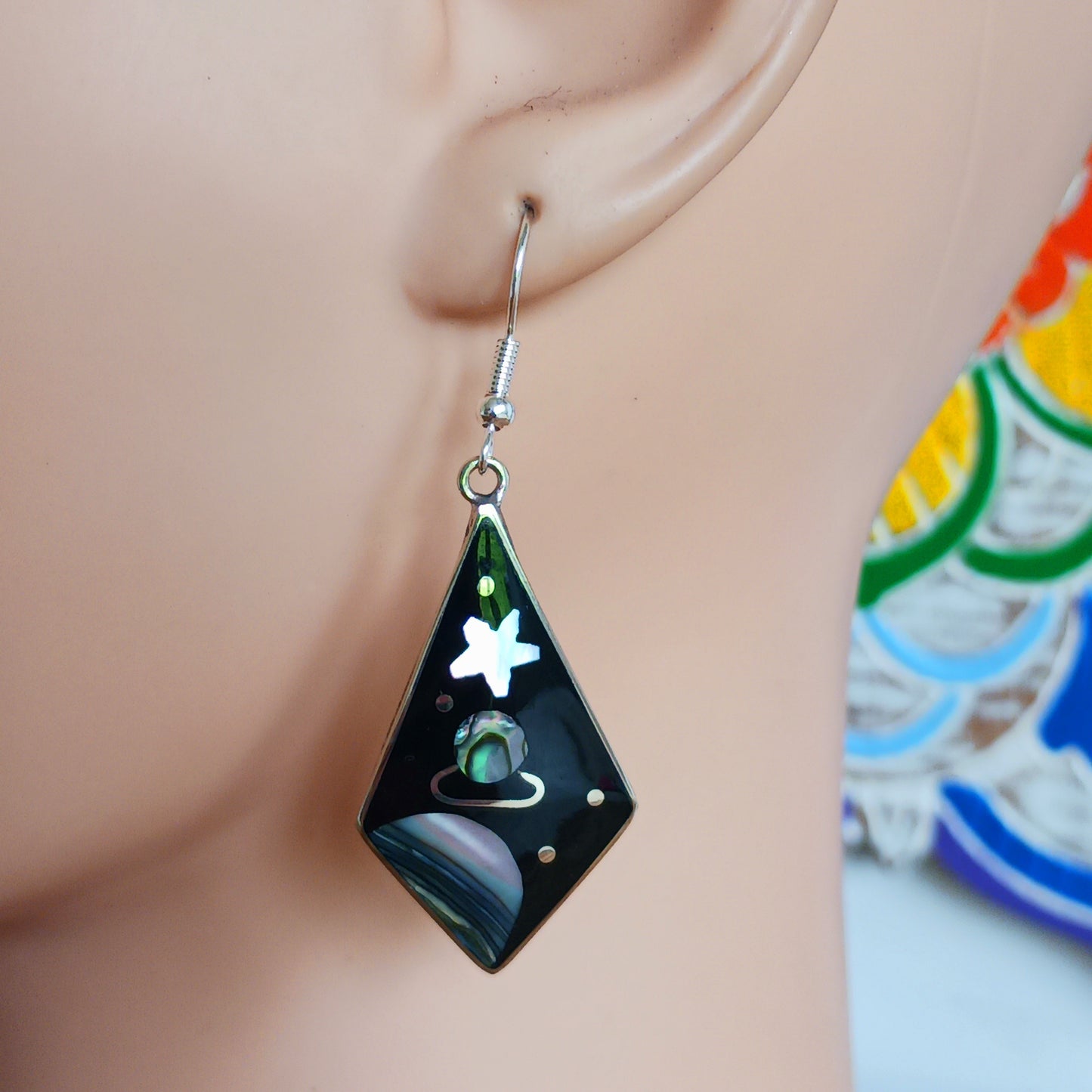 These large diamond shaped earrings feature a cosmic space scene of stars, moons and the planet Saturn crafted from mesmerising abalone shell.