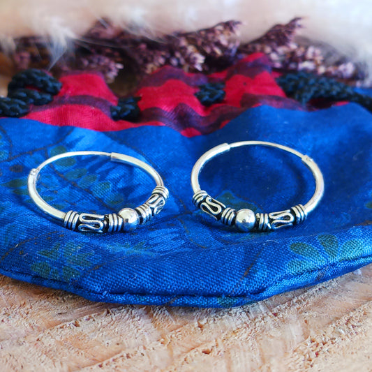 These sterling silver hoop earrings showcase a stunning Bali-inspired design, perfect for adding a touch of elegance to your boho-chic style. The intricate craftsmanship features a delicate silver ball accent at the center of each hoop, embodying a timeless and versatile aesthetic.