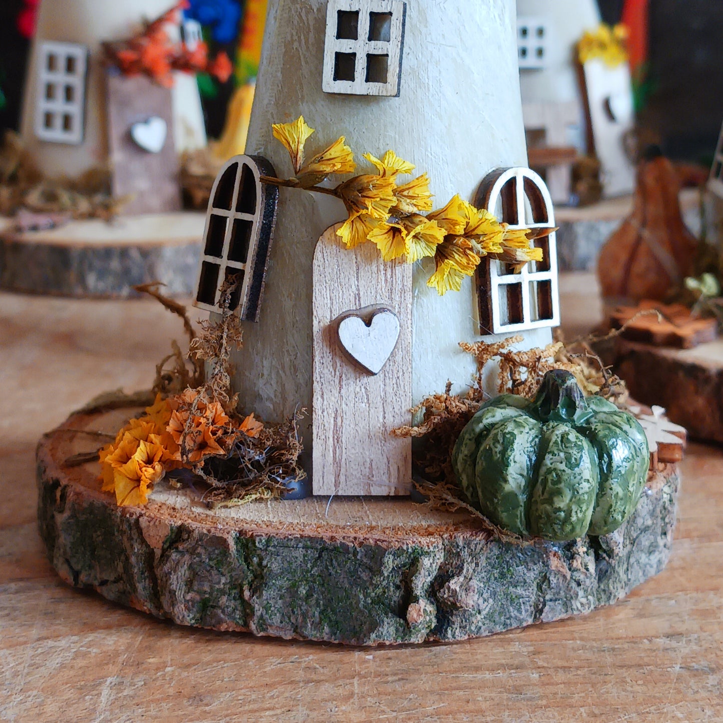 Decorative miniature house with pumpkins and flowers on a wooden base
