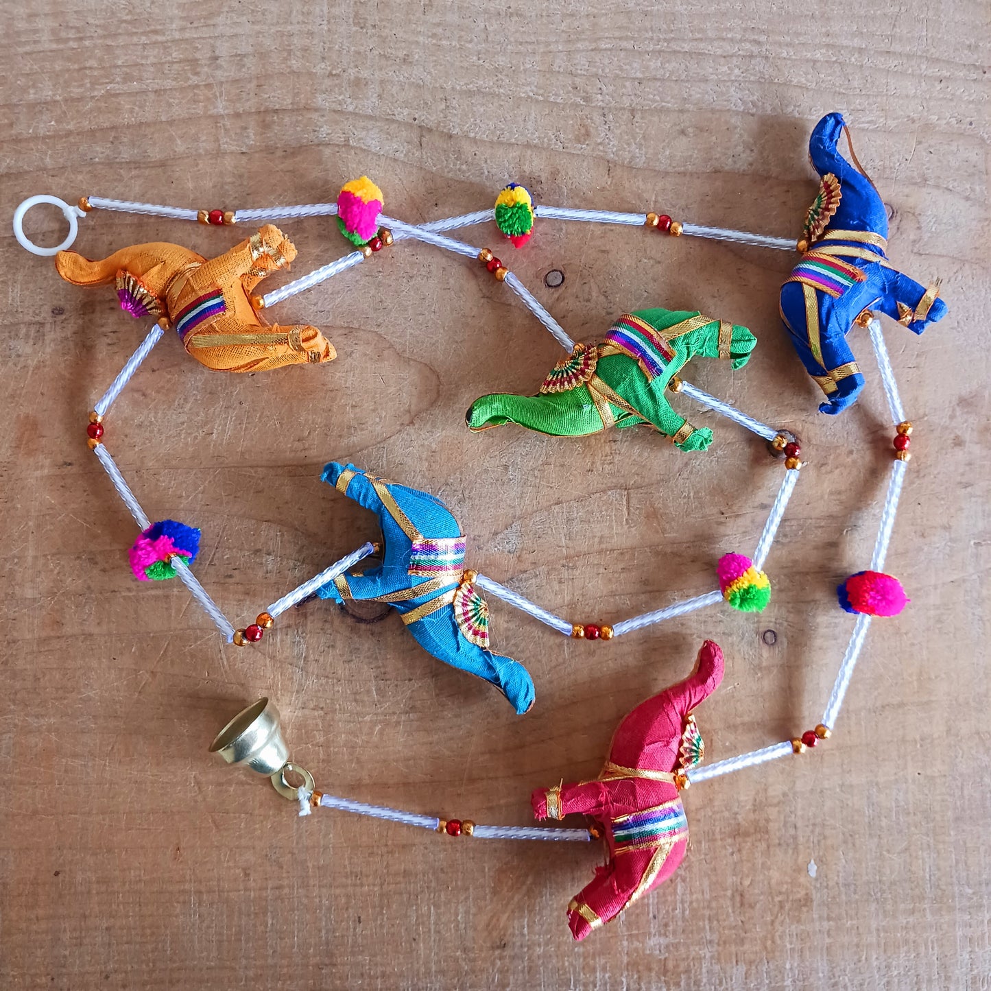 Bring vibrant charm and a touch of global-inspired décor into your home with this beautifully handcrafted stuffed elephant hanging garland. Designed in a traditional tota bell style, this decorative piece features a string of brightly coloured fabric elephants, carefully interspersed with playful beads, mini pom-poms, and delicate jingly bells.