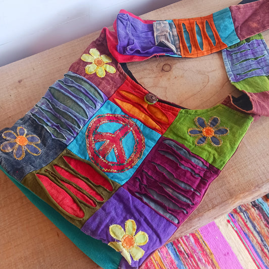 This lovely colourful bag has a hippy design with CND and flower patches. The inside of the spacious shoulder bag is lined with black cotton and there is also a convenient pouch on the strap to pop your phone. The top is secured with a coconut button. These lovely bags are made using up scraps of fabric that would otherwise be wasted. This means that each item is unique.