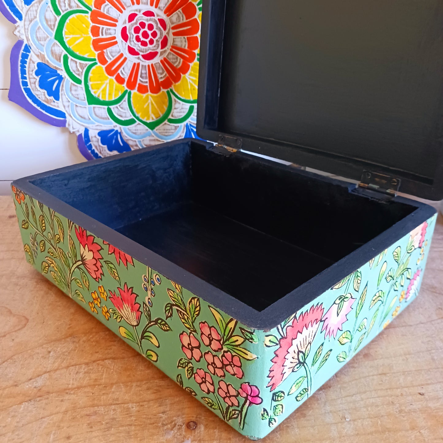 The Saanvi Handcrafted Large Wooden Box is a sustainable gift of beauty, designed to bring charm and practicality to any space. Expertly hand-painted in a bright mixed floral pattern on a pale blue background, this decorative box exudes artisanal elegance. The hinged lid is accented with a small gold-colored knob for a refined touch, while the deep midnight interior offers ample storage for trinkets, jewellery, and cherished keepsakes.