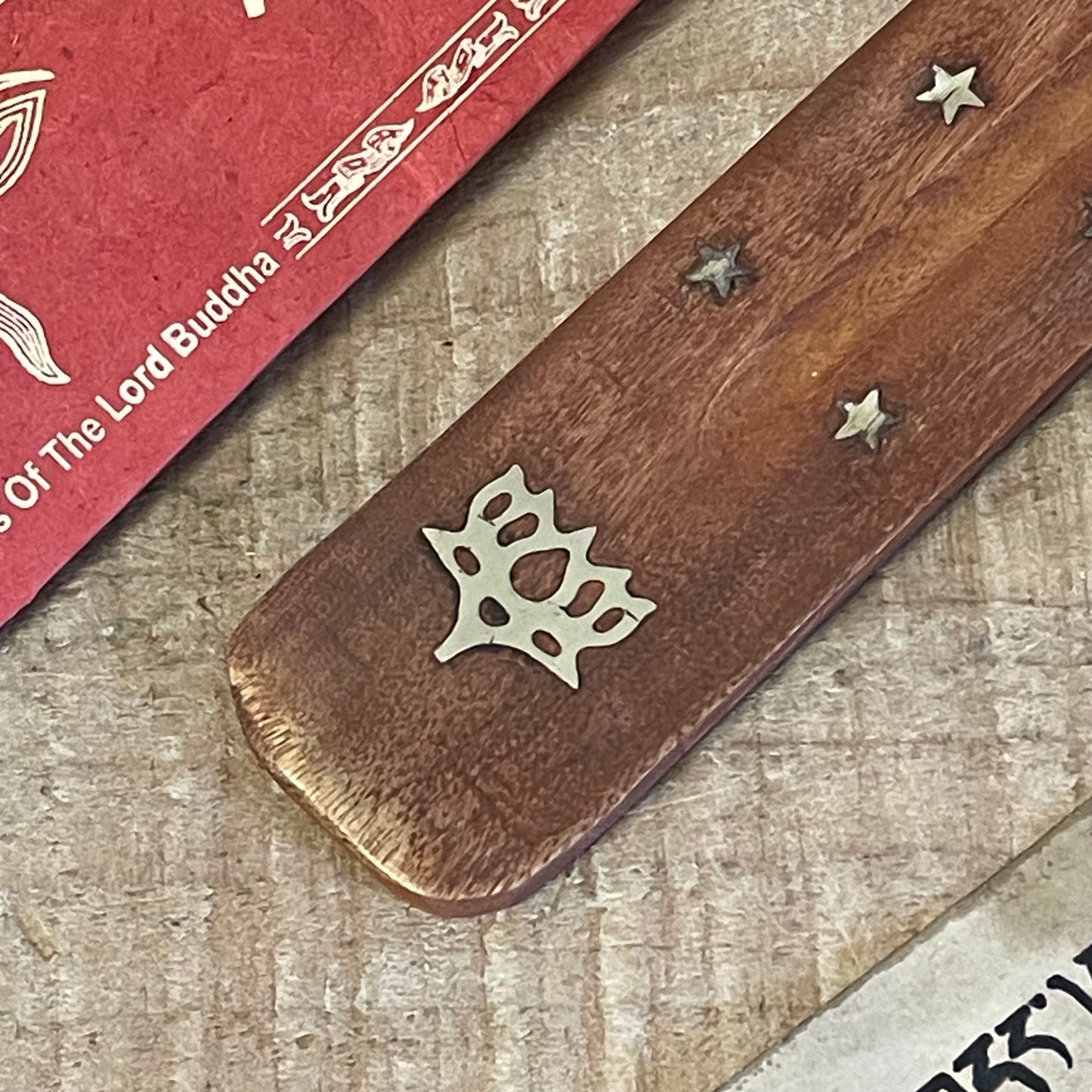 This best-selling incense holder features a unique shoehorn shape, crafted from durable mango wood and designed as an effective ash catcher. Inlaid with brass stars and a lotus flower, this piece adds a touch of elegance and spirituality to any space. The long, slightly curved design holds incense sticks securely, allowing ash to collect neatly along the wooden body for easy cleanup.