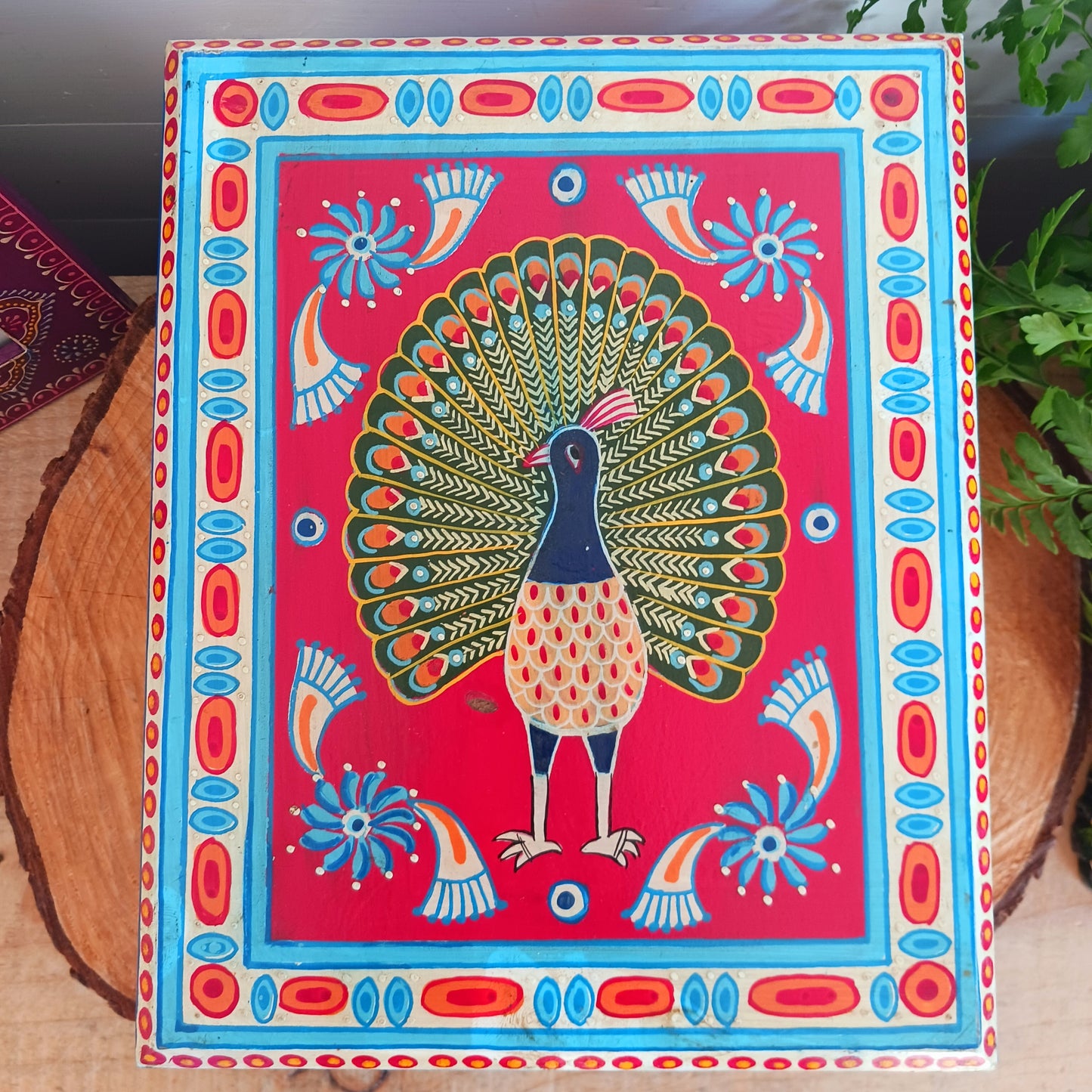 A beautiful peacock design, hand painted jewellery box in a palette of regal reds and blues made from sustainable mango wood.  This lovely box comprises a top opening section with mirror, and a single drawer; two useful compartments, accessed with discreet round knobs.