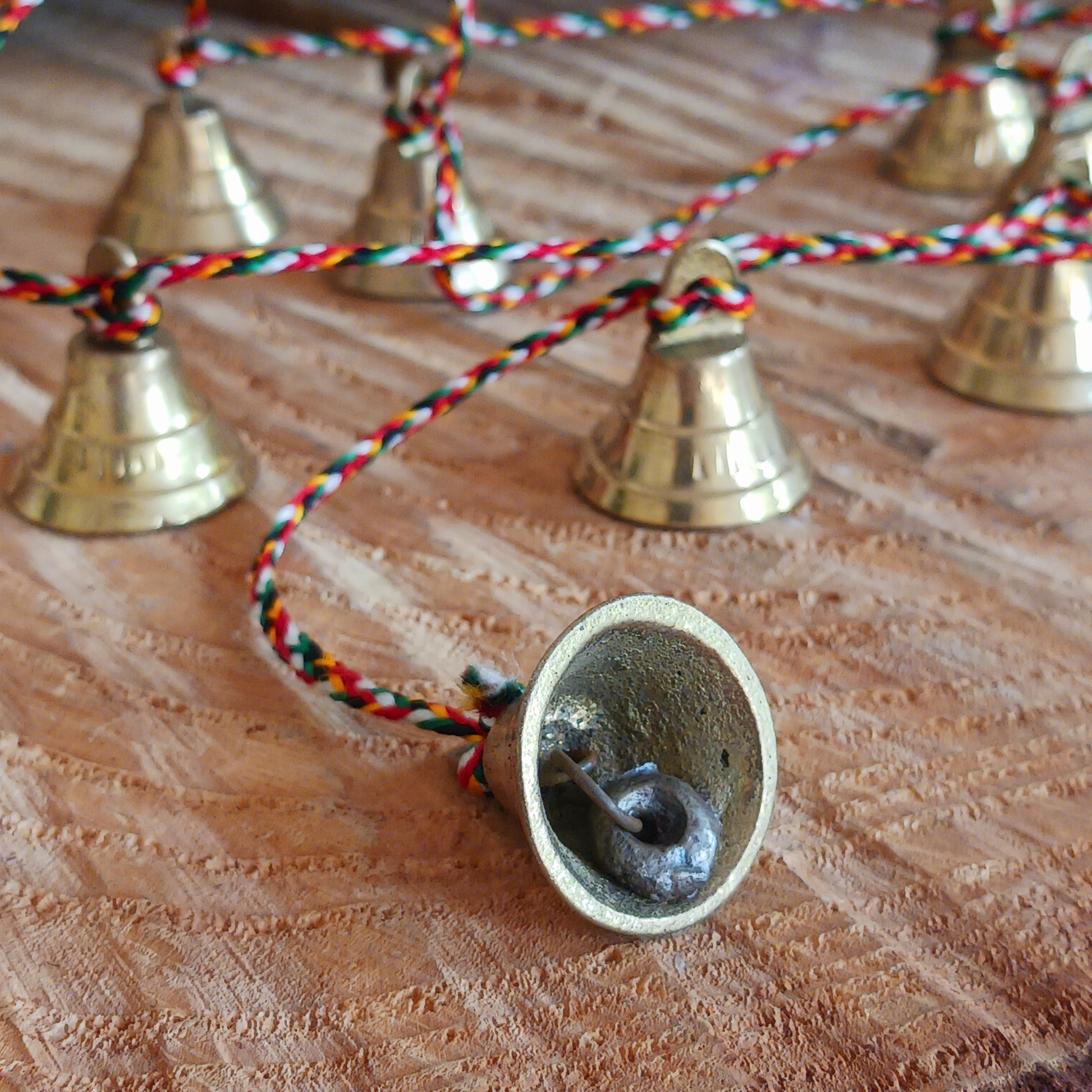 This delightful string of eleven Indian brass bells, hung on a length of rainbow coloured cord. This lovely little string of bells makes a wonderful gentle jingle sound when hung in the breeze.