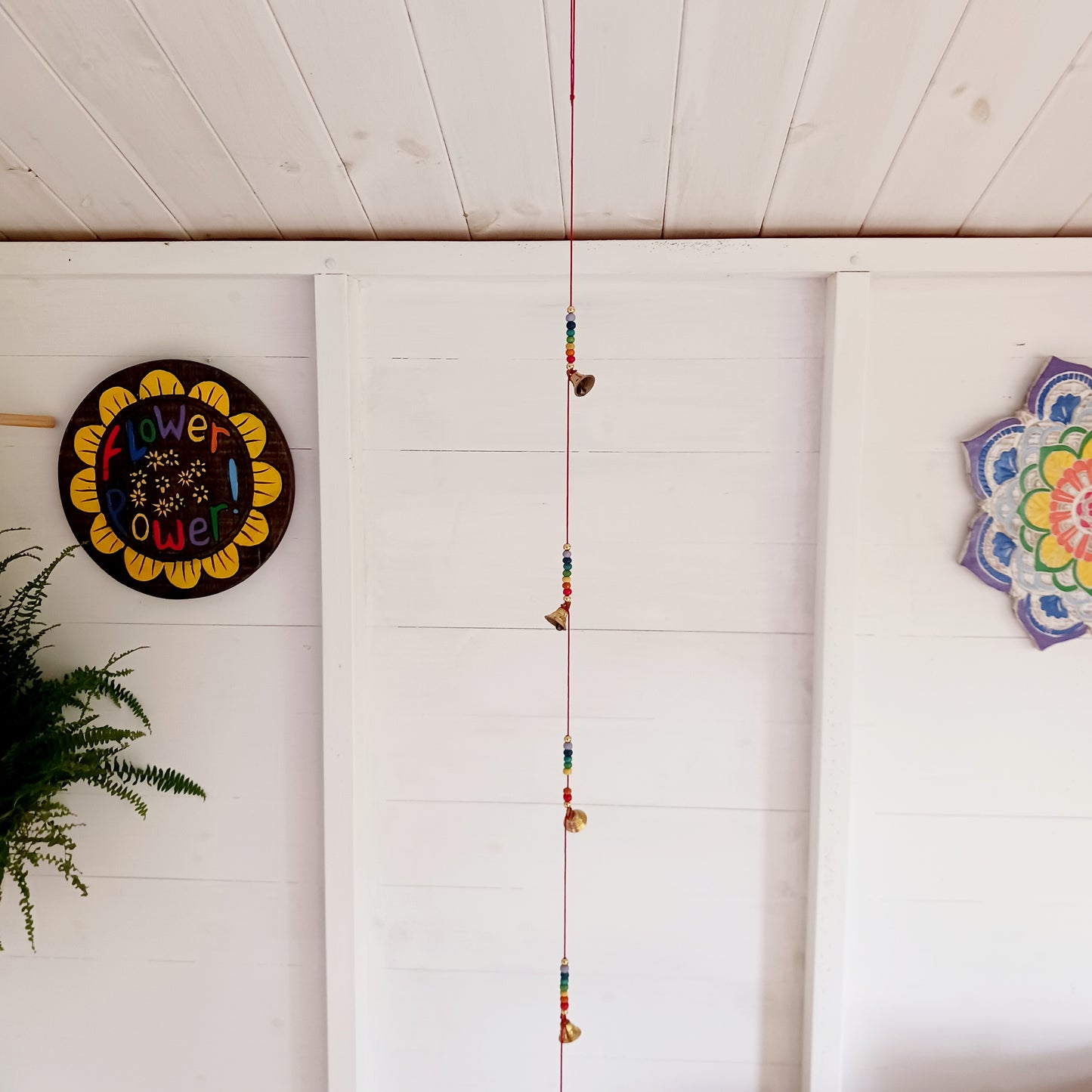 This delightful string of five Indian brass bells, hung on a length of cord have vibrant rainbow colour wooden beads. This lovely little string of bells makes a wonderful gentle jingle sound when hung in the breeze.