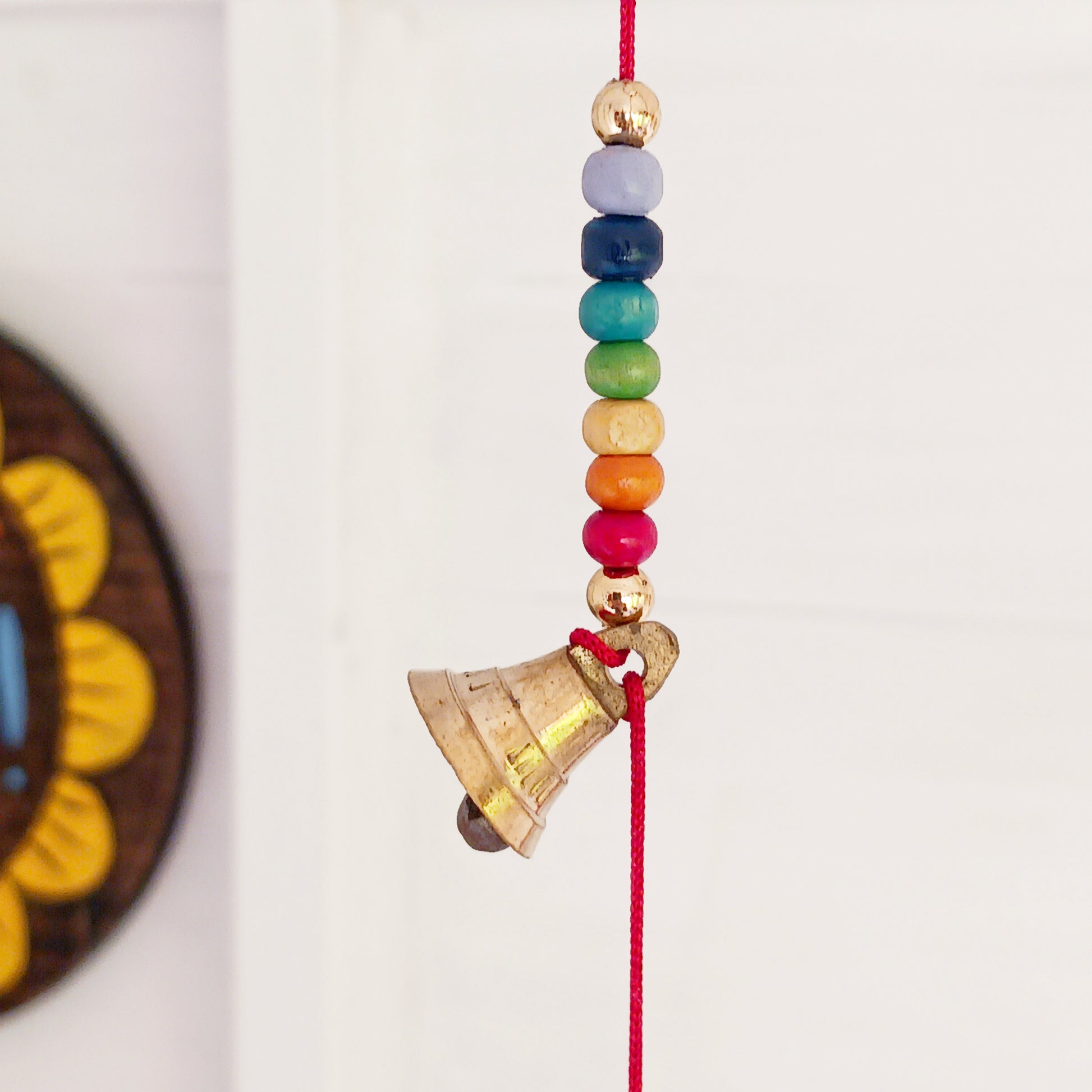 This delightful string of five Indian brass bells, hung on a length of cord have vibrant rainbow colour wooden beads. This lovely little string of bells makes a wonderful gentle jingle sound when hung in the breeze.