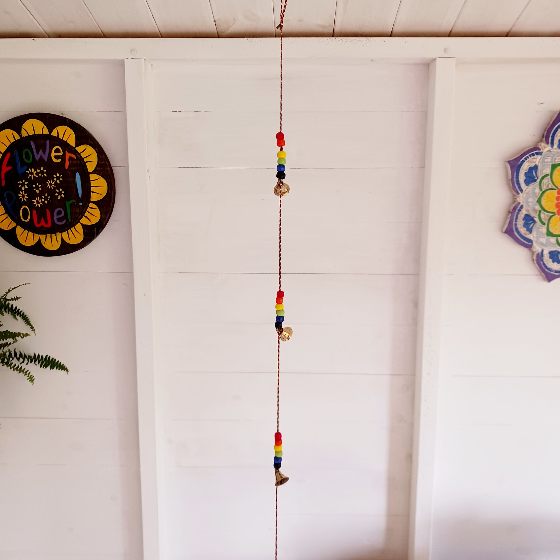 This delightful string of five Indian brass bells, hung on a length of cord have vibrant multi colour wooden beads. This lovely little string of bells makes a wonderful gentle jingle sound when hung in the breeze.