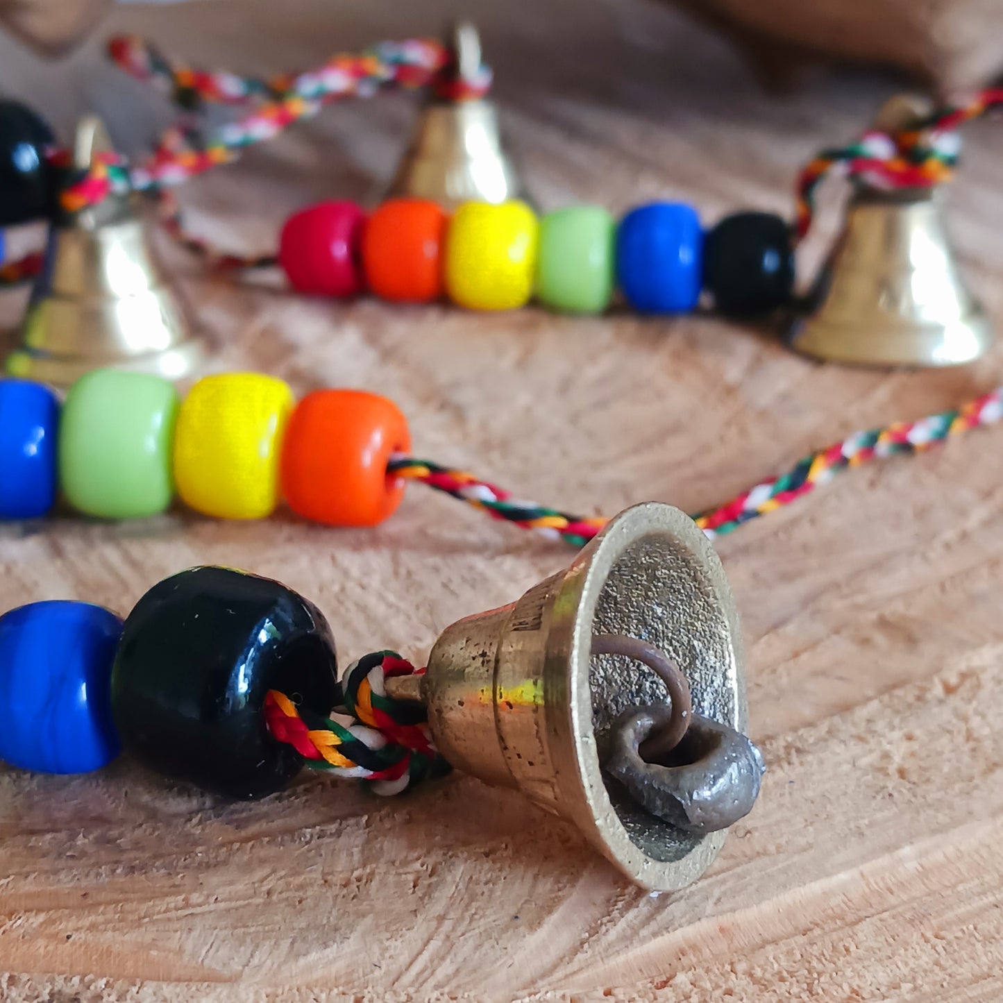 This delightful string of five Indian brass bells, hung on a length of cord have vibrant multi colour wooden beads. This lovely little string of bells makes a wonderful gentle jingle sound when hung in the breeze.