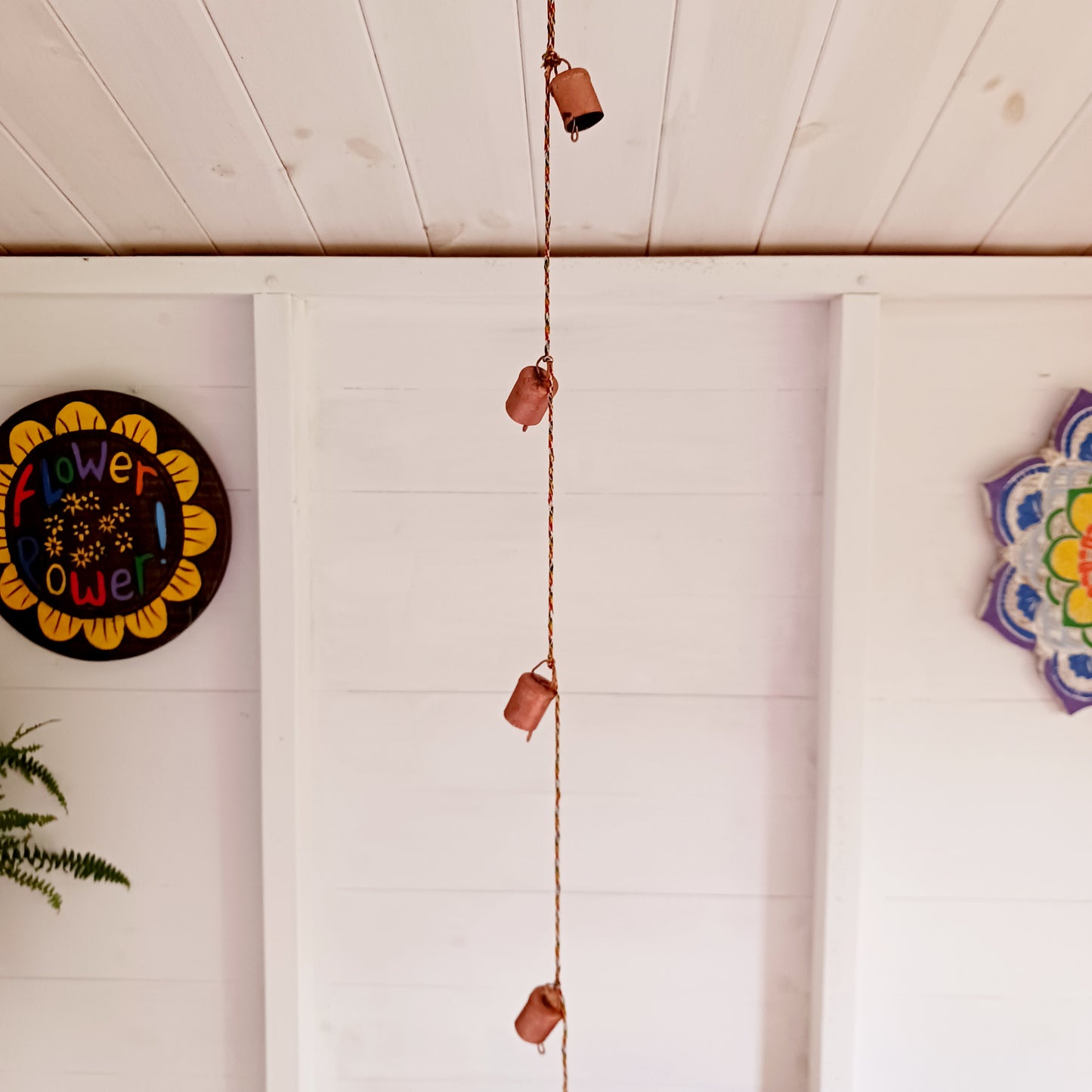 String of small rustic handmade ironwork bells with copper coloured paintwork, hung on a length of colourful string. Each bell has a small metal clapper which produces a gentle tinkling sound.