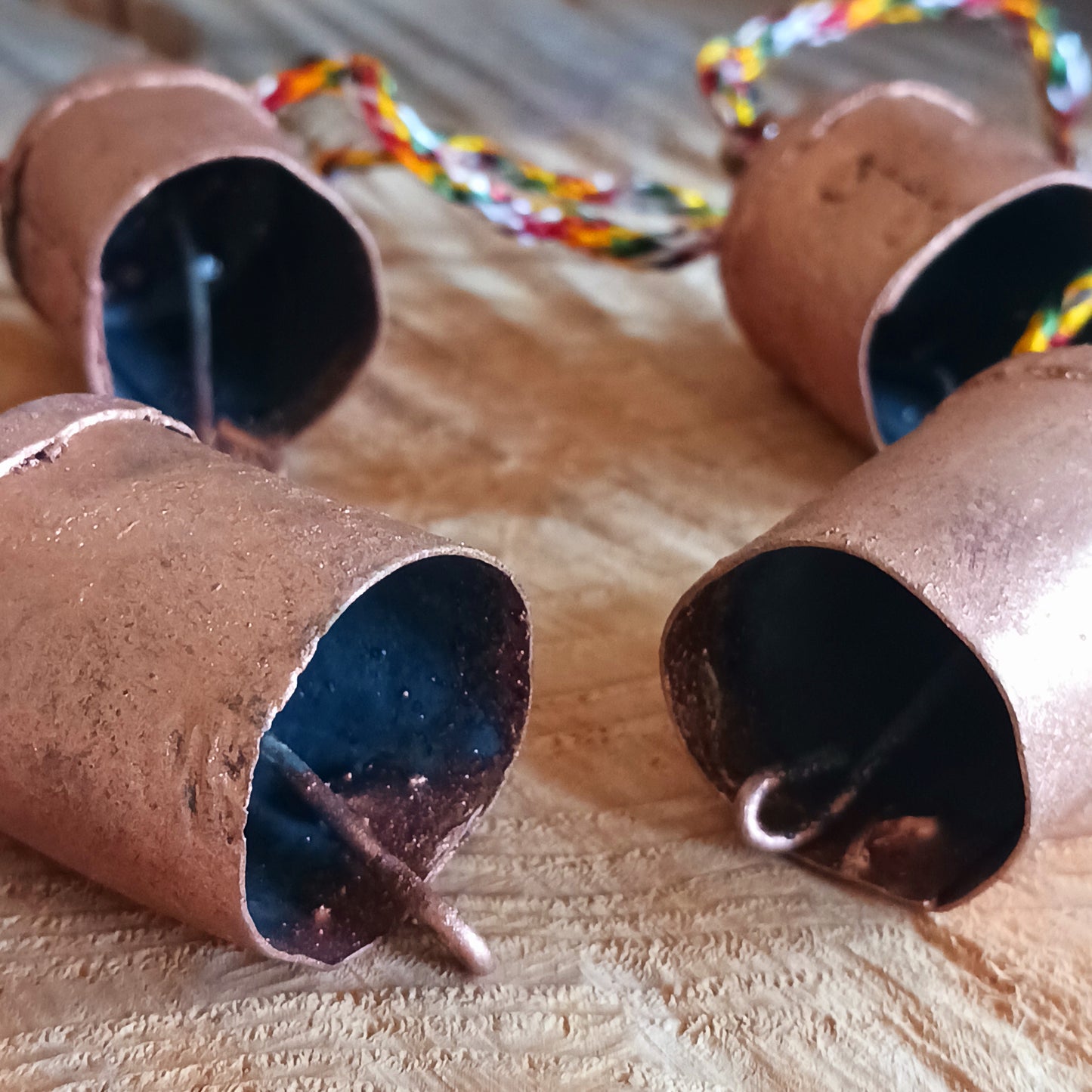 String of small rustic handmade ironwork bells with copper coloured paintwork, hung on a length of colourful string. Each bell has a small metal clapper which produces a gentle tinkling sound.