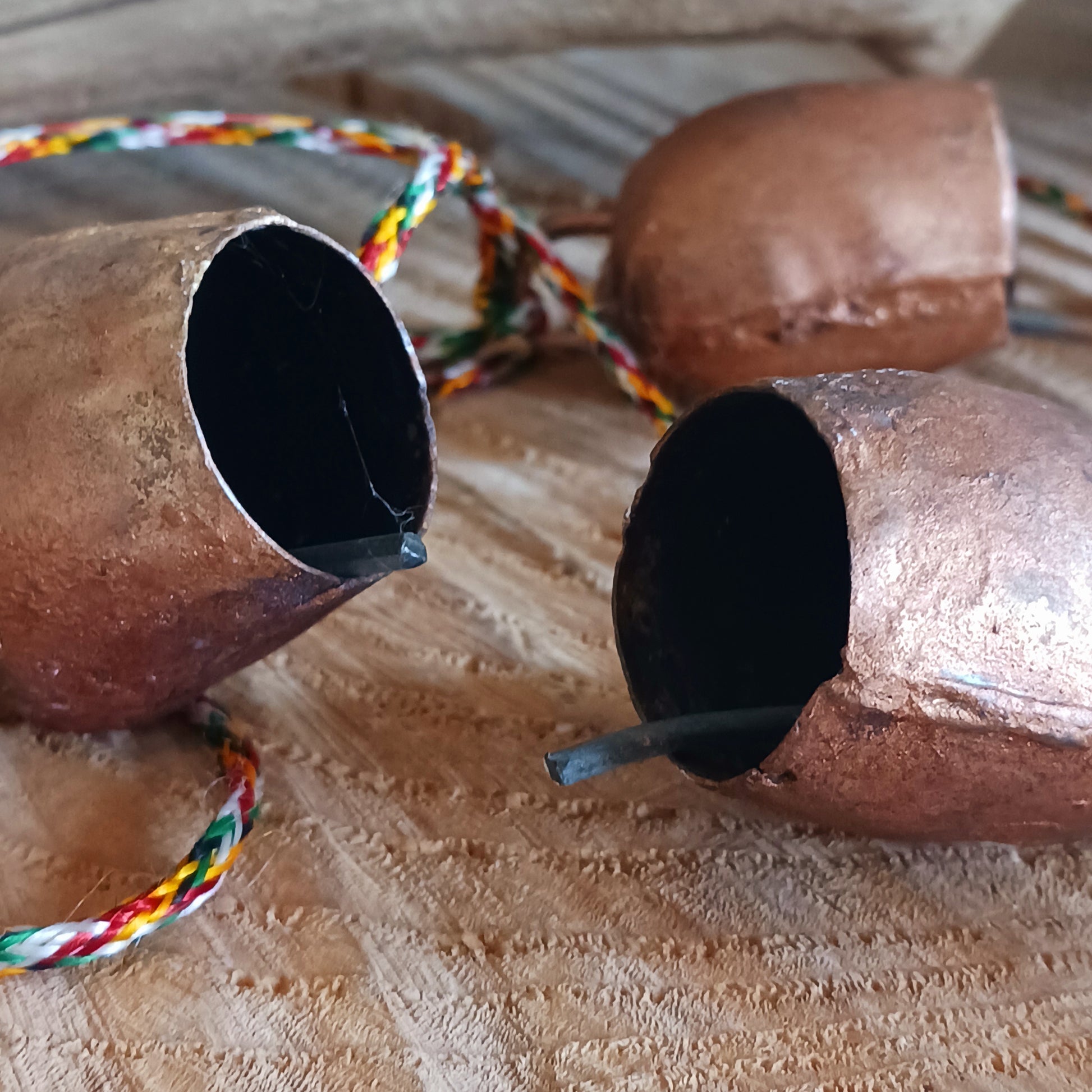 String of small rustic handmade ironwork bells with copper coloured paintwork, hung on a length of colourful string. Each bell has a small metal clapper which produces a gentle tinkling sound.