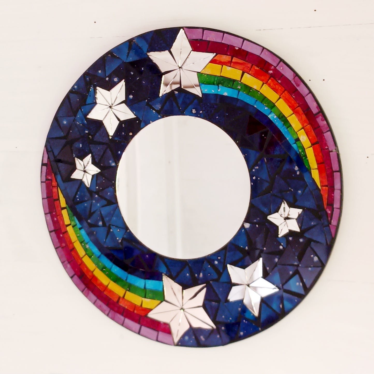 This bright and decorative round mirror is adorned with colourful mosaics creating a wonderful design of rainbow shooting stars flying through the night sky. The central area is a full mirror. Perfect to brighten up any room.