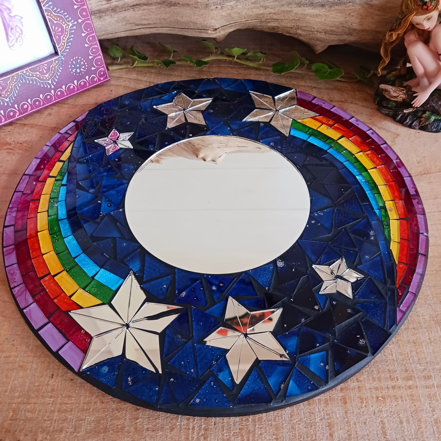 This bright and decorative round mirror is adorned with colourful mosaics creating a wonderful design of rainbow shooting stars flying through the night sky. The central area is a full mirror. Perfect to brighten up any room.