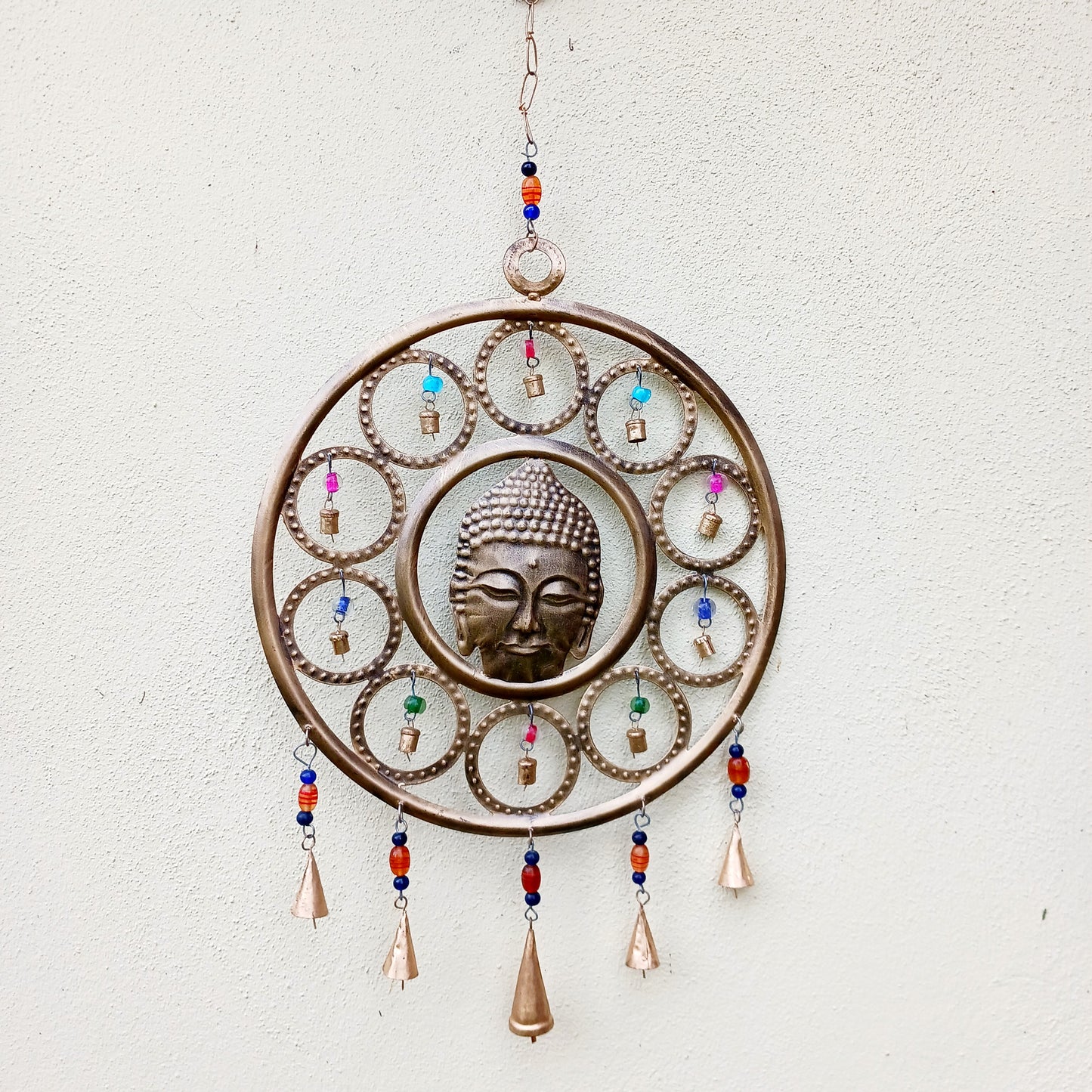 Enhance your living space with this beautiful large Buddha face 15 bell chimes.  This lovely brass decoration exudes serenity and spiritual charm. An intricate piece featuring a serene Buddha face surrounded by delicate circular accents and vibrant, colourful beads. With 15 brass bells, this chime creates a harmonious, soothing sound, making it ideal for both indoor and outdoor spaces.