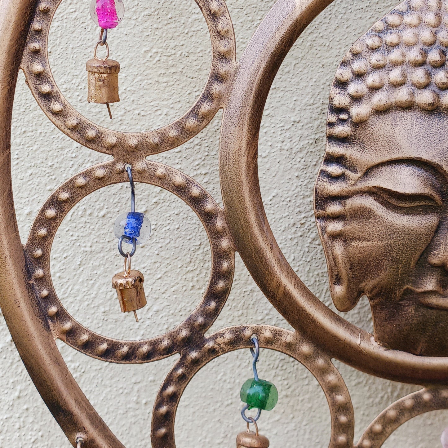 Enhance your living space with this beautiful large Buddha face 15 bell chimes.  This lovely brass decoration exudes serenity and spiritual charm. An intricate piece featuring a serene Buddha face surrounded by delicate circular accents and vibrant, colourful beads. With 15 brass bells, this chime creates a harmonious, soothing sound, making it ideal for both indoor and outdoor spaces.