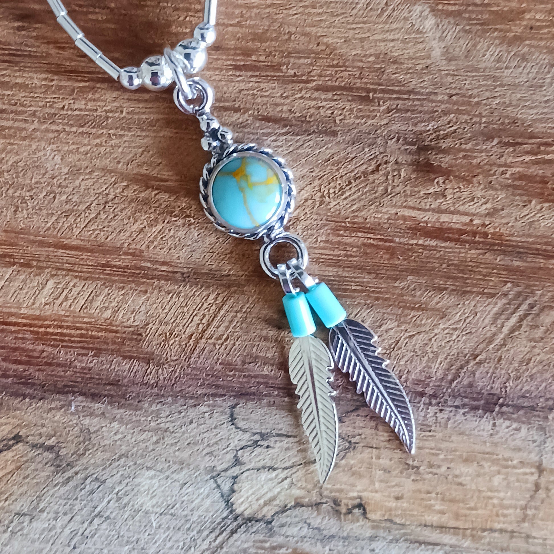 This Turquoise Silver feather necklace is a stunning piece of boho style jewellery featuring an authentic Native American design with a turquoise stone and two silver feathers. This beautiful pendant makes a meaningful gift, blending cultural heritage with personalized elegance.