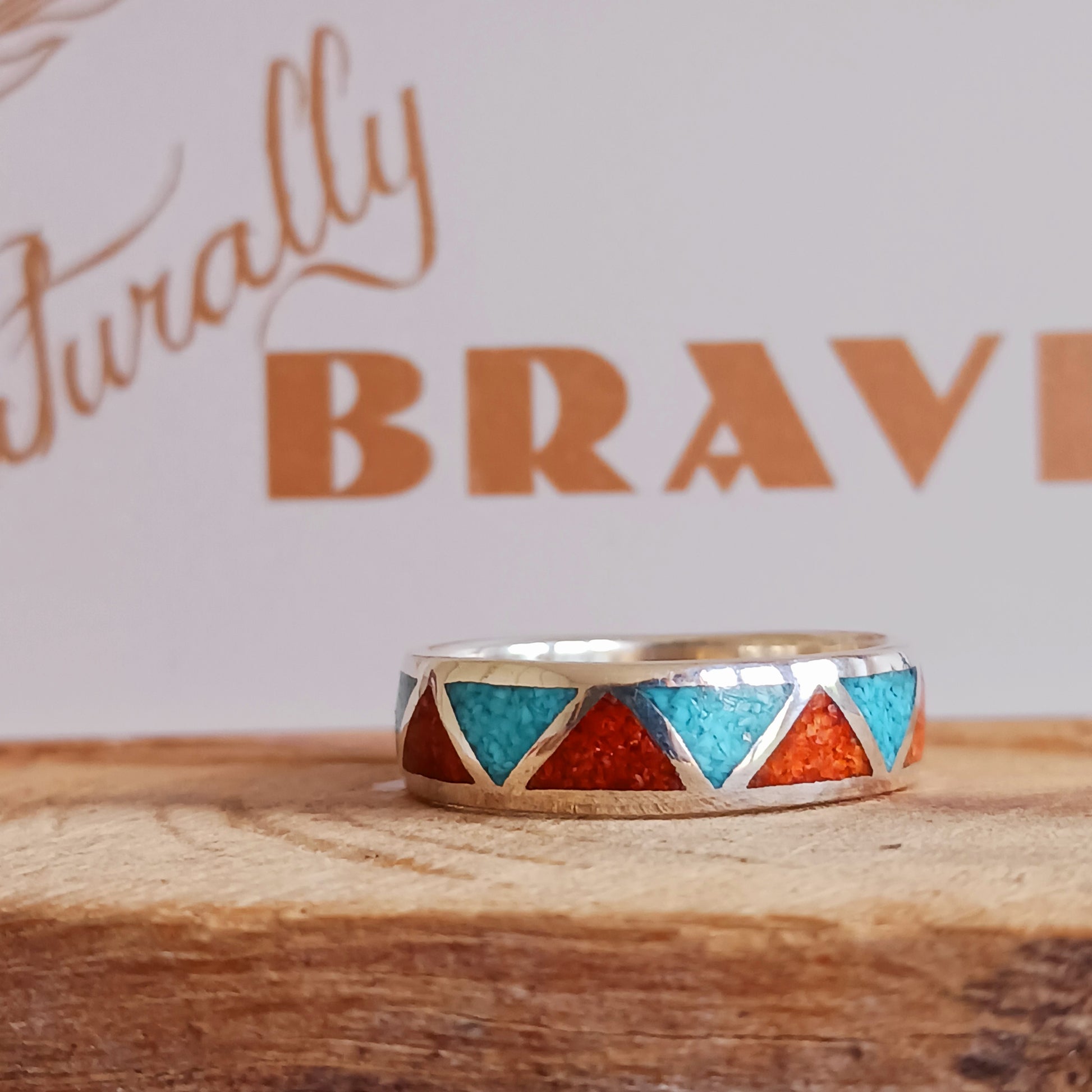 This beautiful inlaid Silver Turquoise Coral Navajo Ring offers a traditional, Native American pattern. Opposing triangles are fitted with hand crushed, gemstone chips. Set in Sterling Silver, this ring offers a smooth flat surface that will fit comfortably on your finger or thumb.  Perfect for his and her bands, this inlaid Silver Turquoise Coral Navajo Ring is a nice contrast for any occasion.