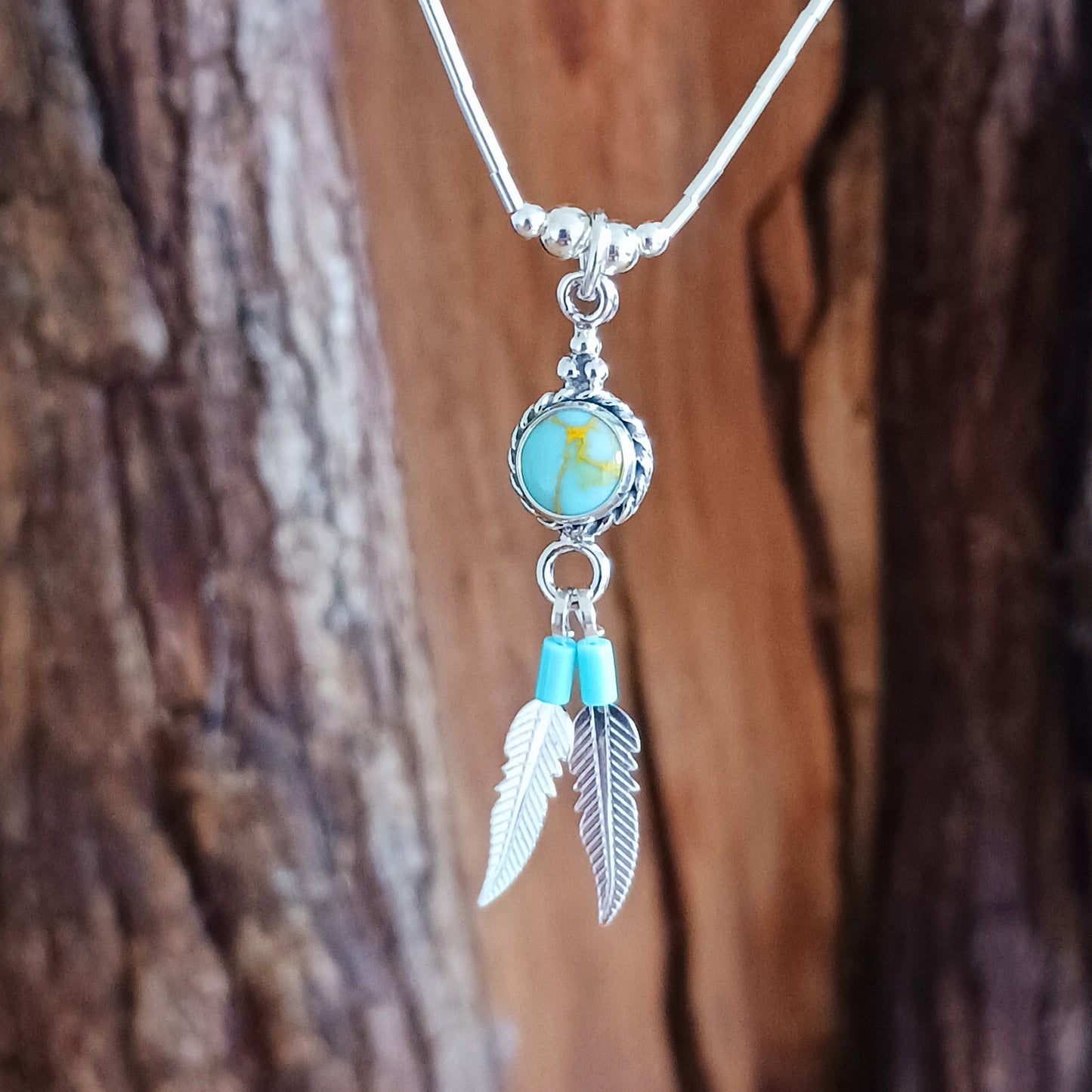 This Turquoise Silver feather necklace is a stunning piece of boho style jewellery featuring an authentic Native American design with a turquoise stone and two silver feathers. This beautiful pendant makes a meaningful gift, blending cultural heritage with personalized elegance.