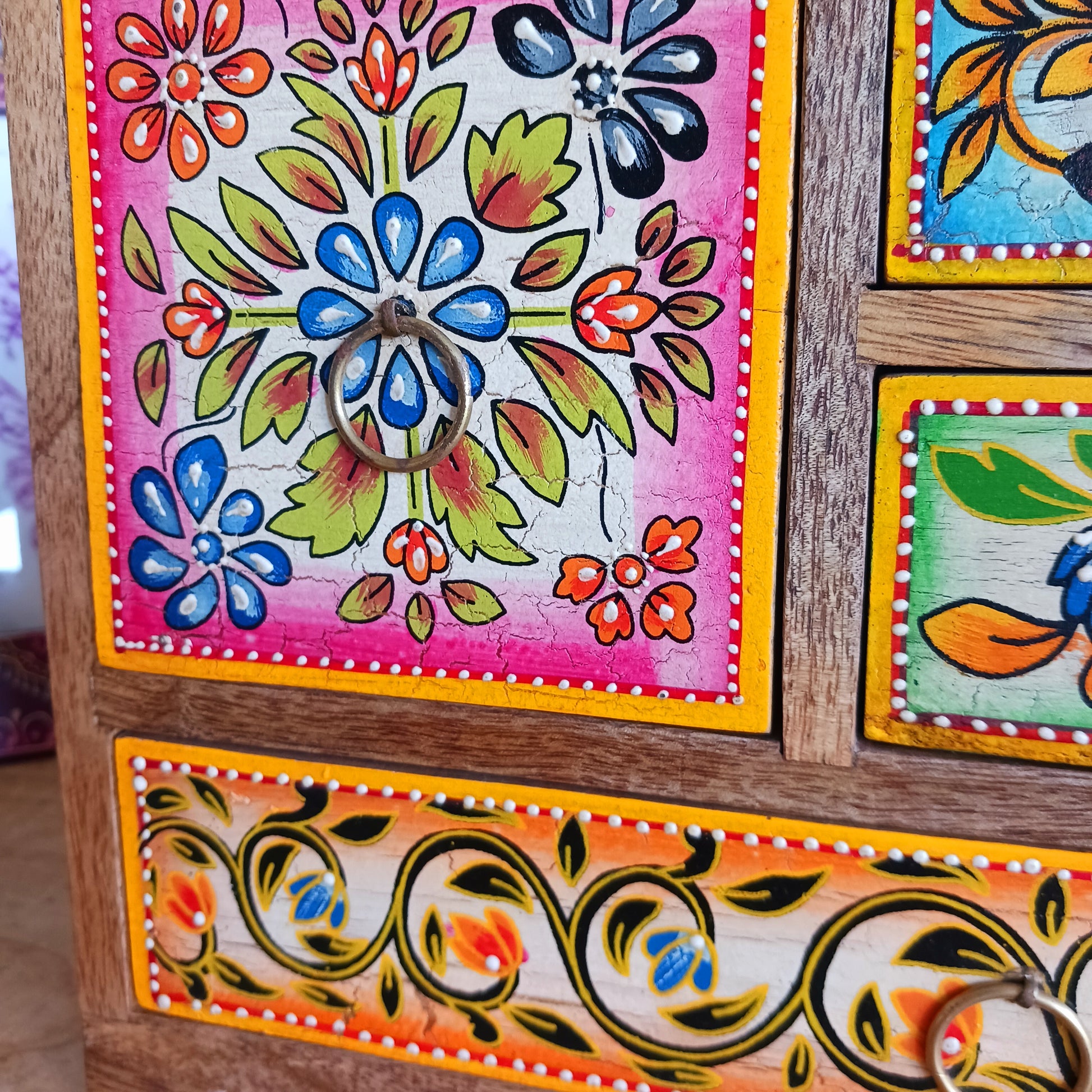 This beautiful Zaha hand painted 4 drawer mango wood chest radiates warmth and charm. Beautiful leafed vines adorn each drawer front in blue, green, red and amber with discreet central ring pull handles in gold colour. Every drawer pane is emboldened in crisp painted beading and amber.