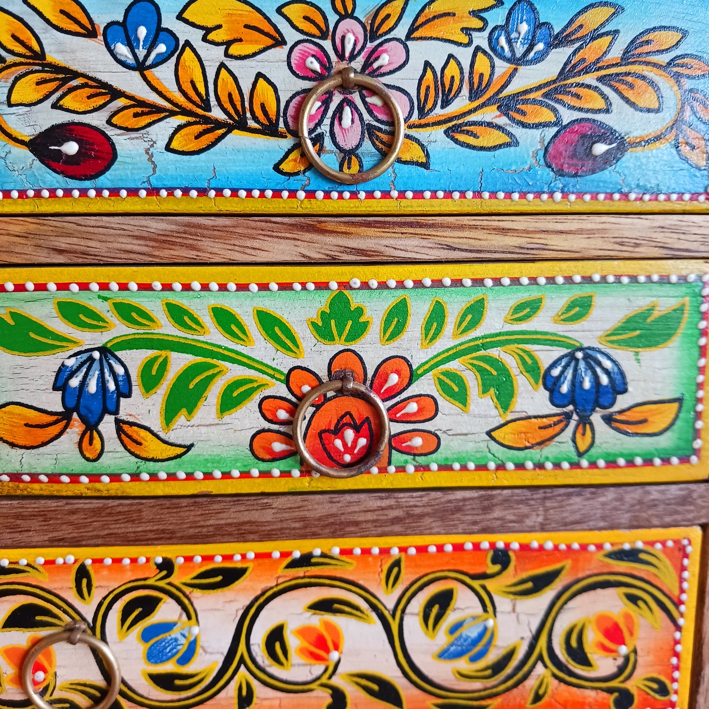 This beautiful Zaha hand painted 4 drawer mango wood chest radiates warmth and charm. Beautiful leafed vines adorn each drawer front in blue, green, red and amber with discreet central ring pull handles in gold colour. Every drawer pane is emboldened in crisp painted beading and amber.