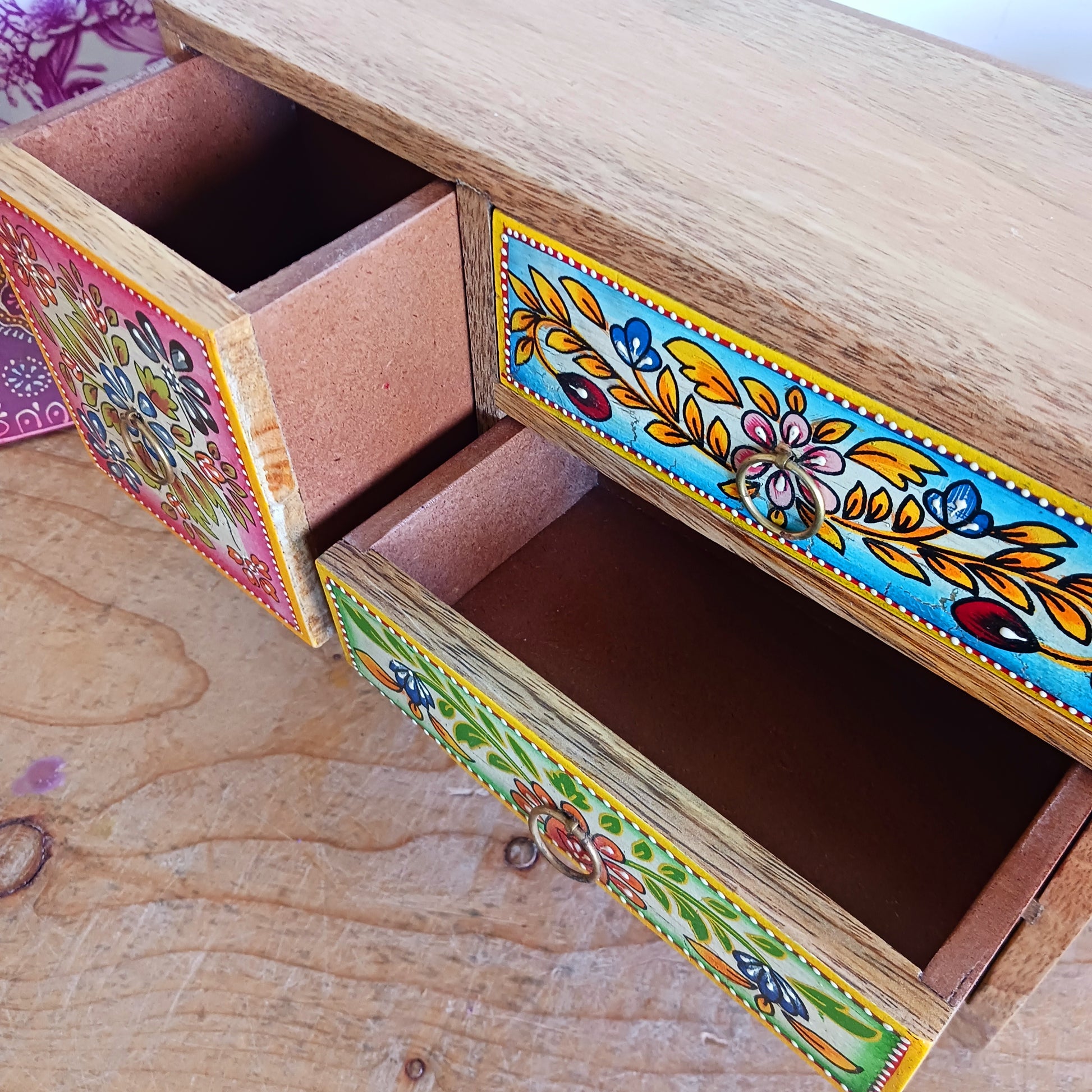 This beautiful Zaha hand painted 4 drawer mango wood chest radiates warmth and charm. Beautiful leafed vines adorn each drawer front in blue, green, red and amber with discreet central ring pull handles in gold colour. Every drawer pane is emboldened in crisp painted beading and amber.