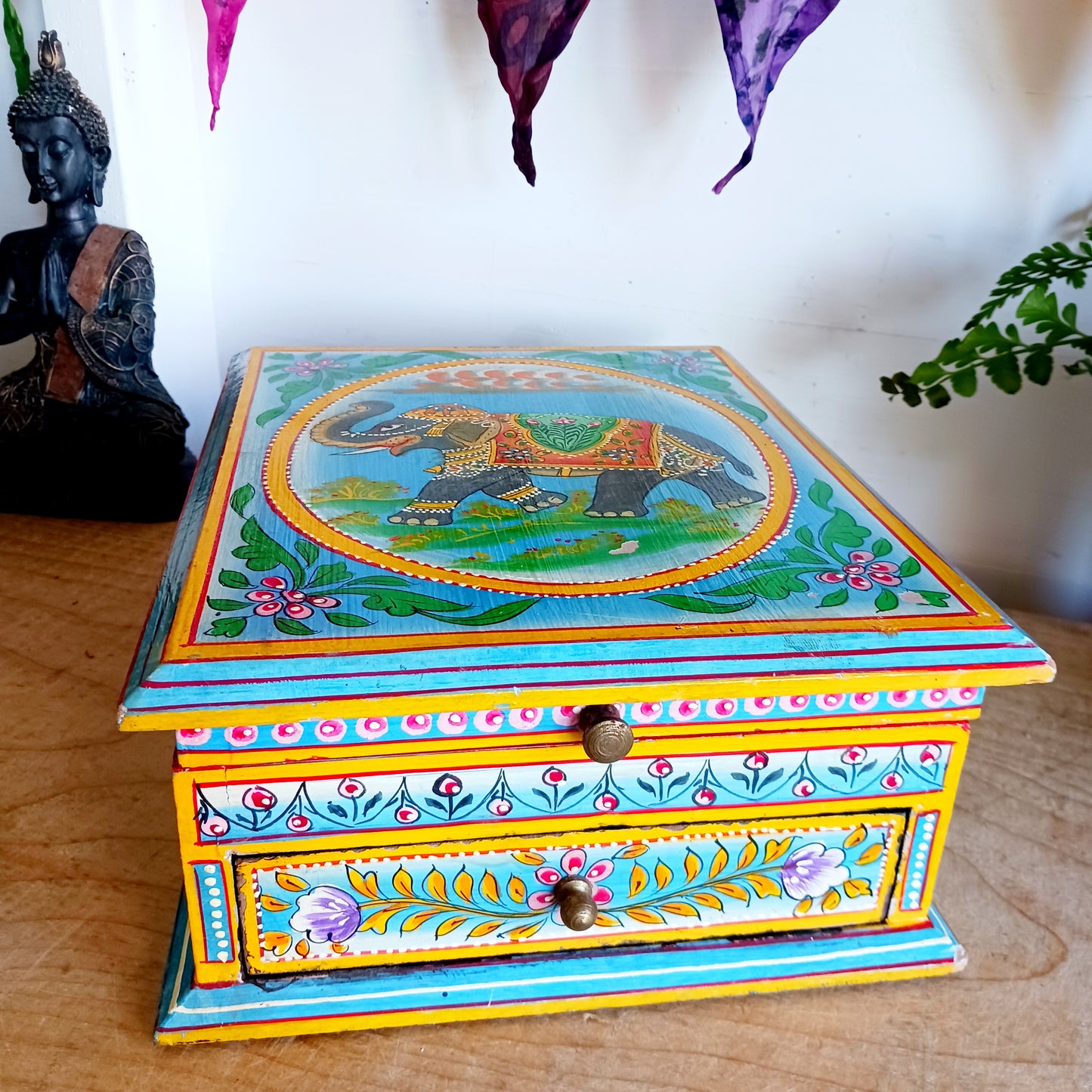 This stunning large Indian jewellery box has been hand painted to perfection in fresh spring-like colours of pastel blue, primrose yellow, pale pink and new season green.&nbsp; The elephant on the lid is in full ceremonial regalia and oval framed in yellow. It comprises a single drawer and top compartment opened by discreet round knobs.  A beautiful addition to any home.