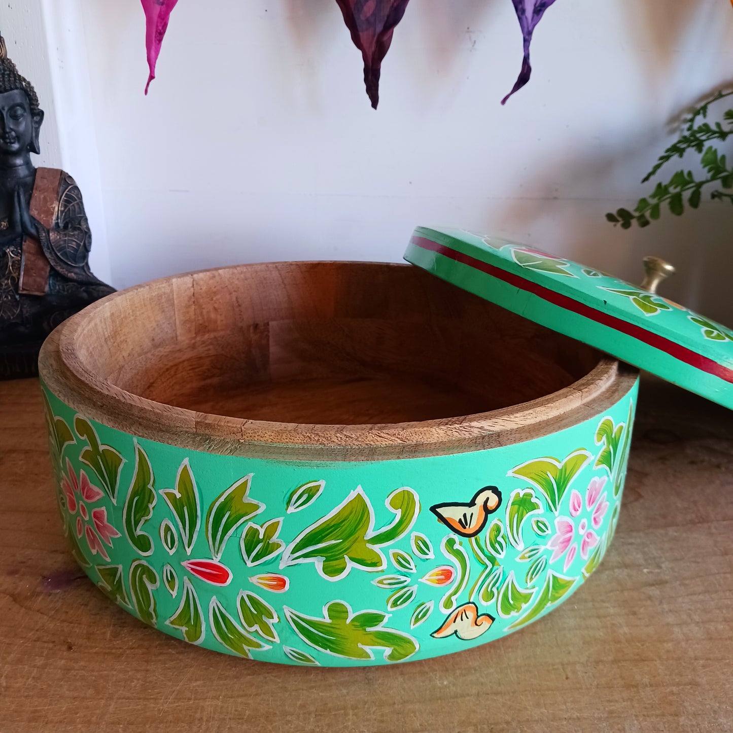 This beautiful large turquoise round Indian wooden box has been hand painted in a peacock design on the pull-off lid. It has a small round gold coloured central knob. Green leaves and pink flowers complete an appealing design.