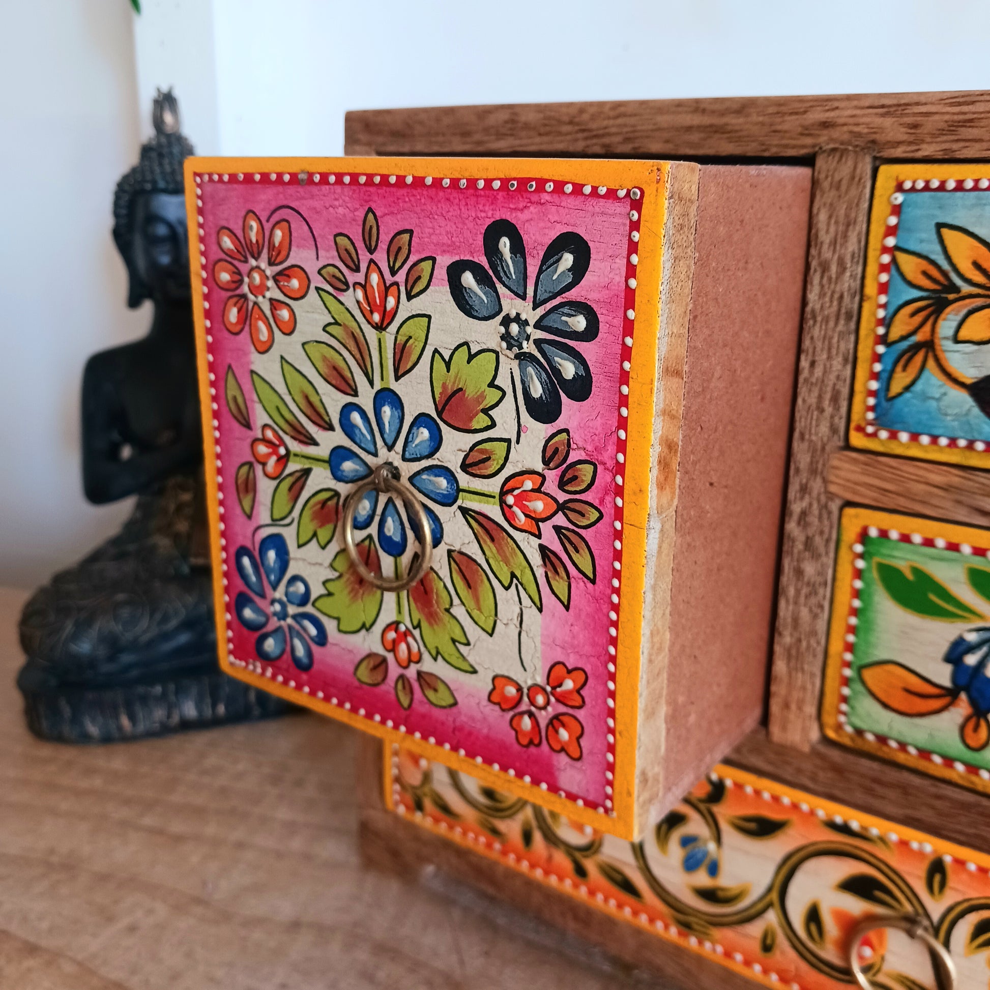 This beautiful Zaha hand painted 4 drawer mango wood chest radiates warmth and charm. Beautiful leafed vines adorn each drawer front in blue, green, red and amber with discreet central ring pull handles in gold colour. Every drawer pane is emboldened in crisp painted beading and amber.