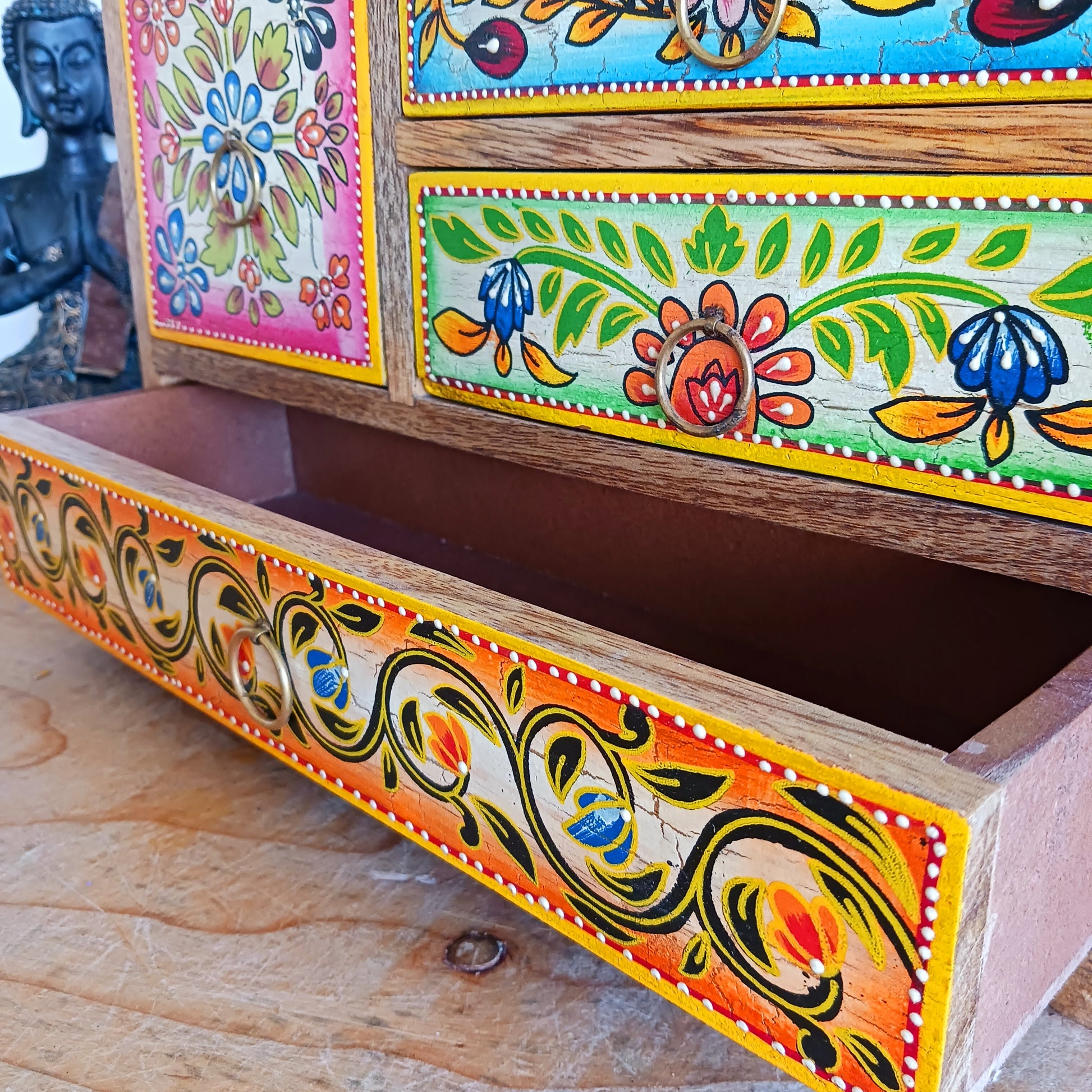 This beautiful Zaha hand painted 4 drawer mango wood chest radiates warmth and charm. Beautiful leafed vines adorn each drawer front in blue, green, red and amber with discreet central ring pull handles in gold colour. Every drawer pane is emboldened in crisp painted beading and amber.