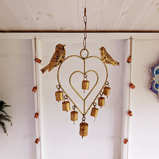 This lovely windchime is features a large metal heart that encloses a smaller heart, that in turn, holds an Indian decorative bell. Perched on the top of the windchime sit a pair of feather detailed birds. The hanging windchime decoration has a mounting chain and is completed by 7 Indian bells on the bottom edge; the largest bell in the centre.