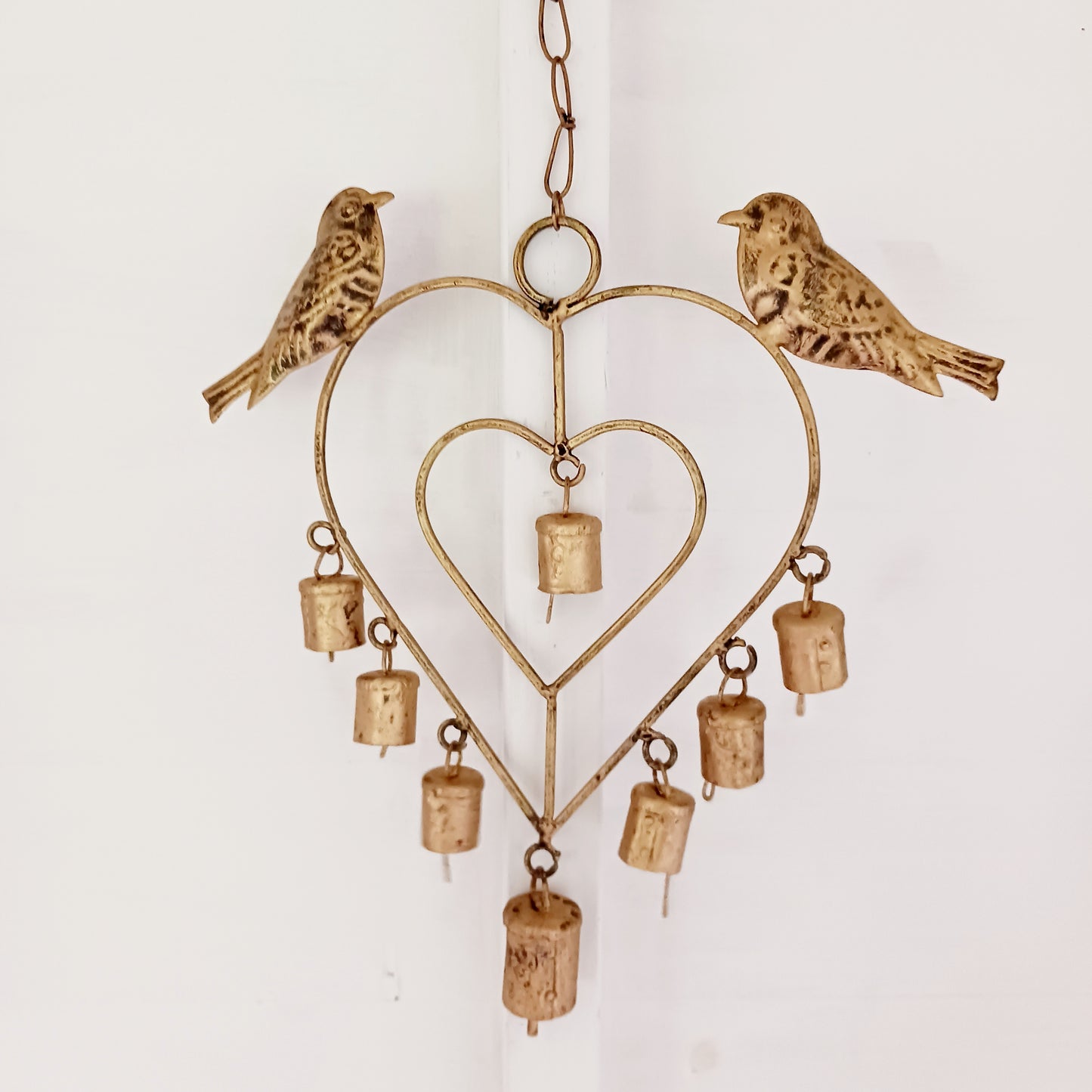 This lovely windchime is features a large metal heart that encloses a smaller heart, that in turn, holds an Indian decorative bell. Perched on the top of the windchime sit a pair of feather detailed birds. The hanging windchime decoration has a mounting chain and is completed by 7 Indian bells on the bottom edge; the largest bell in the centre.