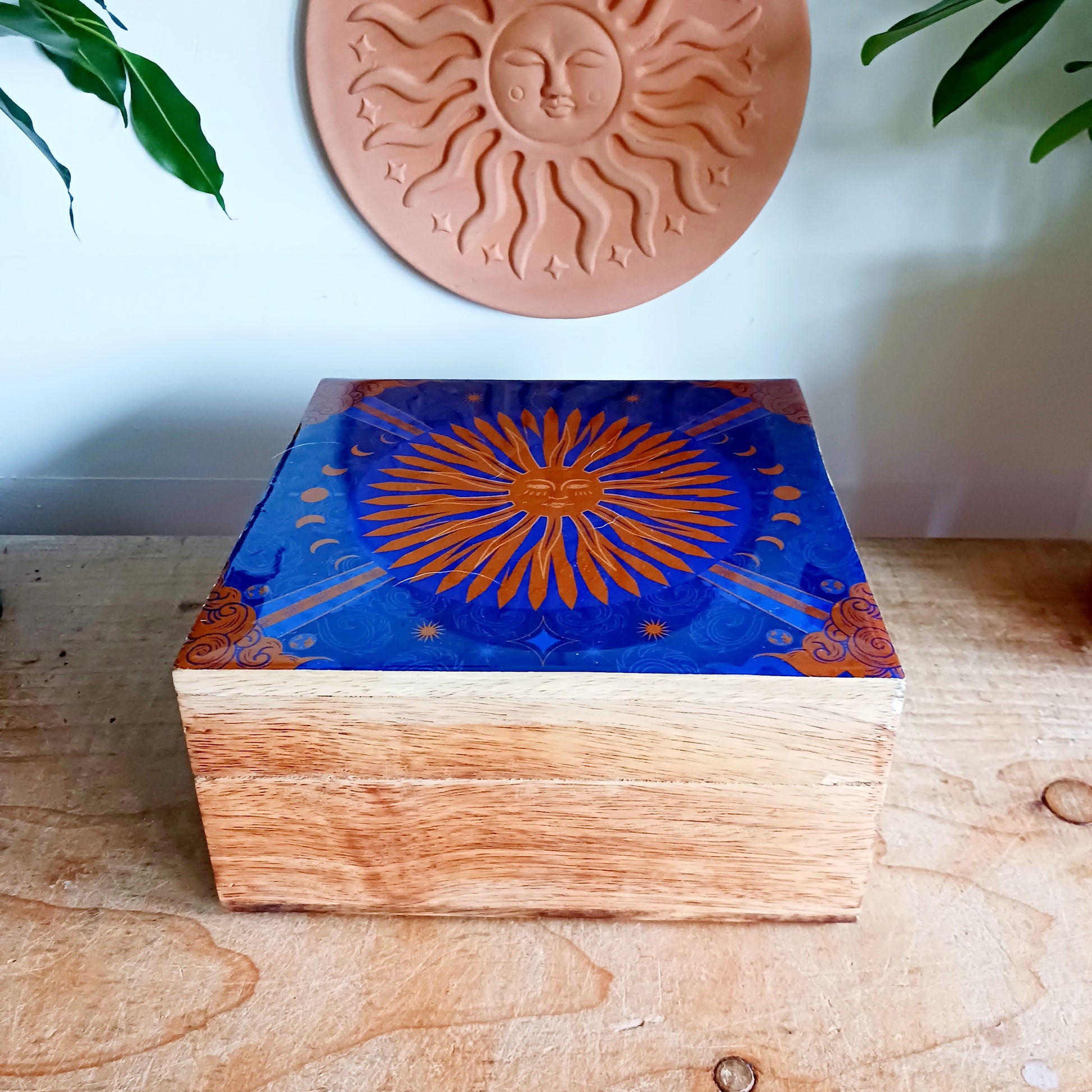 Illuminate your space with the Hop Hare Big Enamelled Square Box, a handcrafted treasure that blends beauty, spirituality, and functionality. Made from sustainable mango wood and adorned with deep blue enamel, this large storage box features a radiant golden sun design symbolizing success, confidence, joy, and vitality.