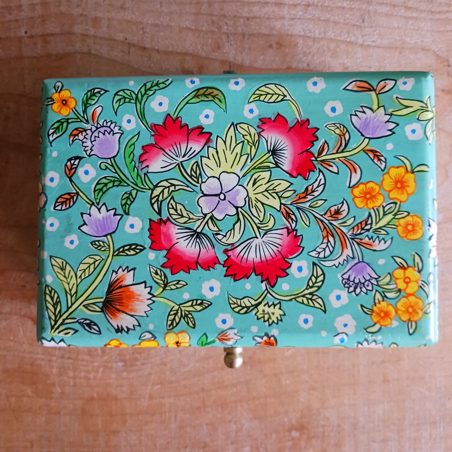The Saanvi Handcrafted Small Wooden Box is a sustainable gift of beauty, designed to bring charm and practicality to any space. Expertly hand-painted in a bright mixed floral pattern on a pale blue background, this decorative box exudes artisanal elegance.