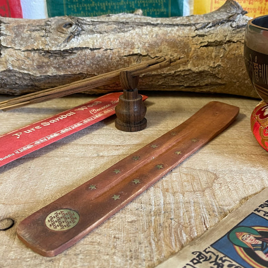 This popular shoehorn-style incense holder, crafted from mango wood, serves as both a beautiful and functional ash catcher. The design is adorned with brass inlays featuring stars and the Flower of Life, a symbol representing the interconnectedness of life. Its long, slightly curved shape securely holds stick incense, with the wooden base effectively catching falling ash to keep surfaces clean.