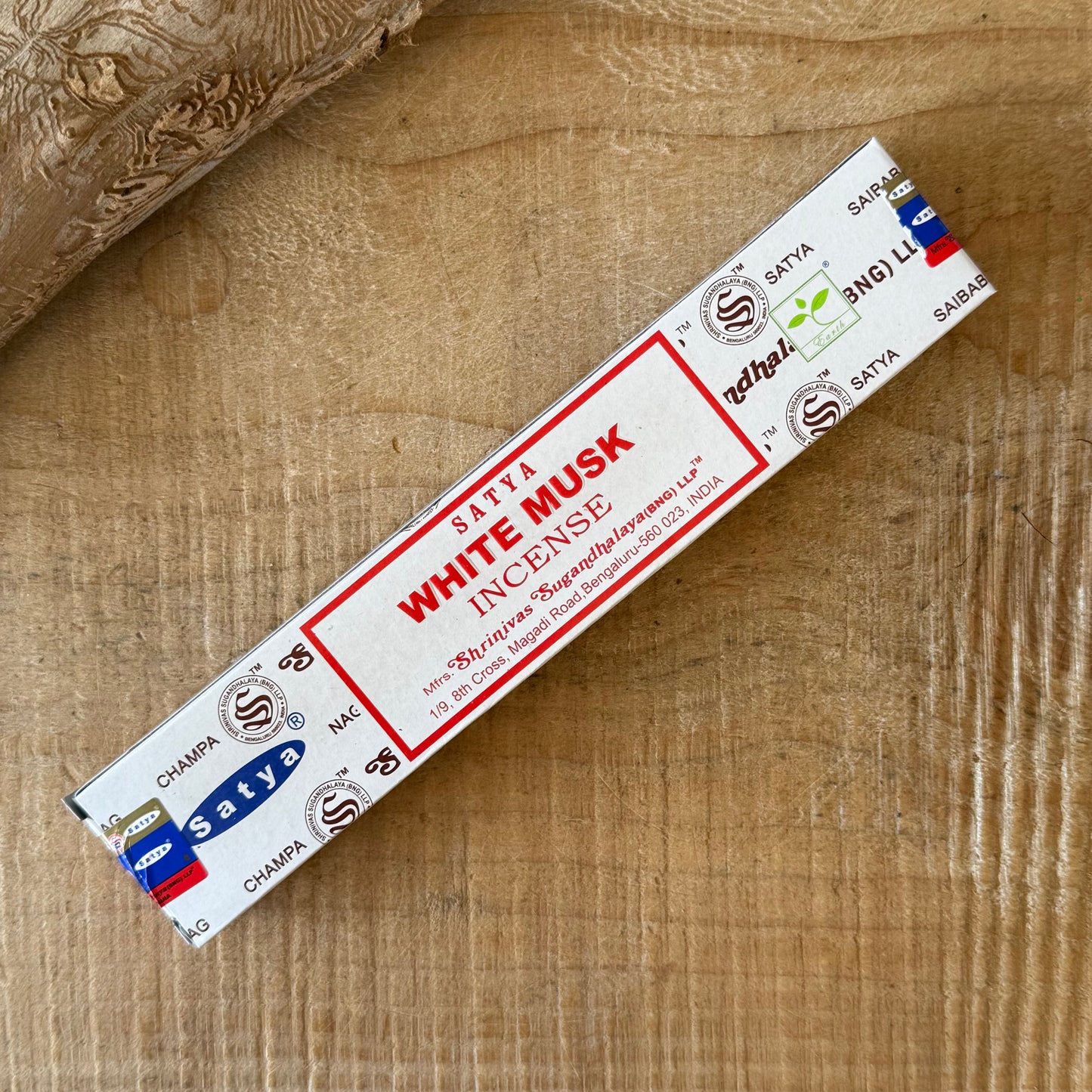 A single stick of Satya White Musk Incense placed diagonally on a light brown wooden surface.
