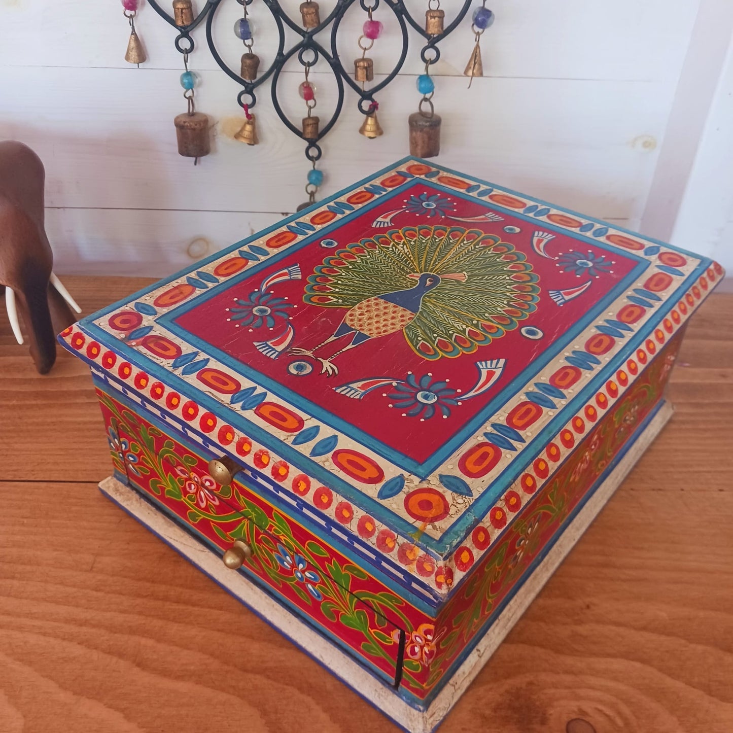 A beautiful peacock design, hand painted jewellery box in a palette of regal reds and blues made from sustainable mango wood.  This lovely box comprises a top opening section with mirror, and a single drawer; two useful compartments, accessed with discreet round knobs.