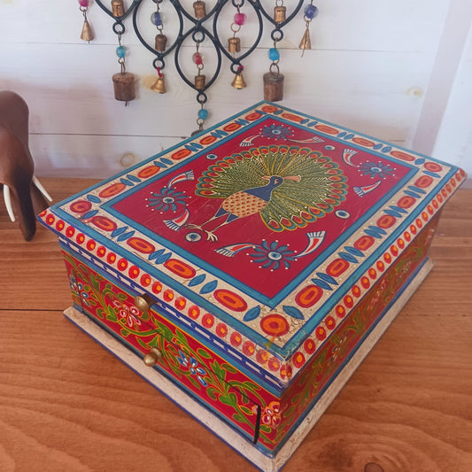 A beautiful peacock design, hand painted jewellery box in a palette of regal reds and blues made from sustainable mango wood.  This lovely box comprises a top opening section with mirror, and a single drawer; two useful compartments, accessed with discreet round knobs.